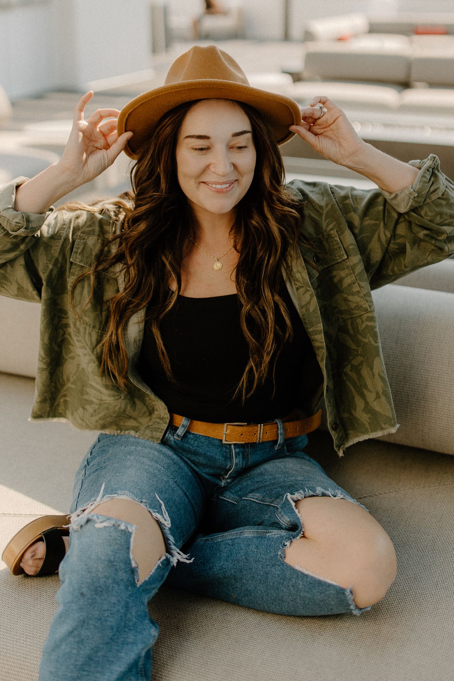 Person wearing a brown hat and camouflage jacket lounges casually on grey furniture.