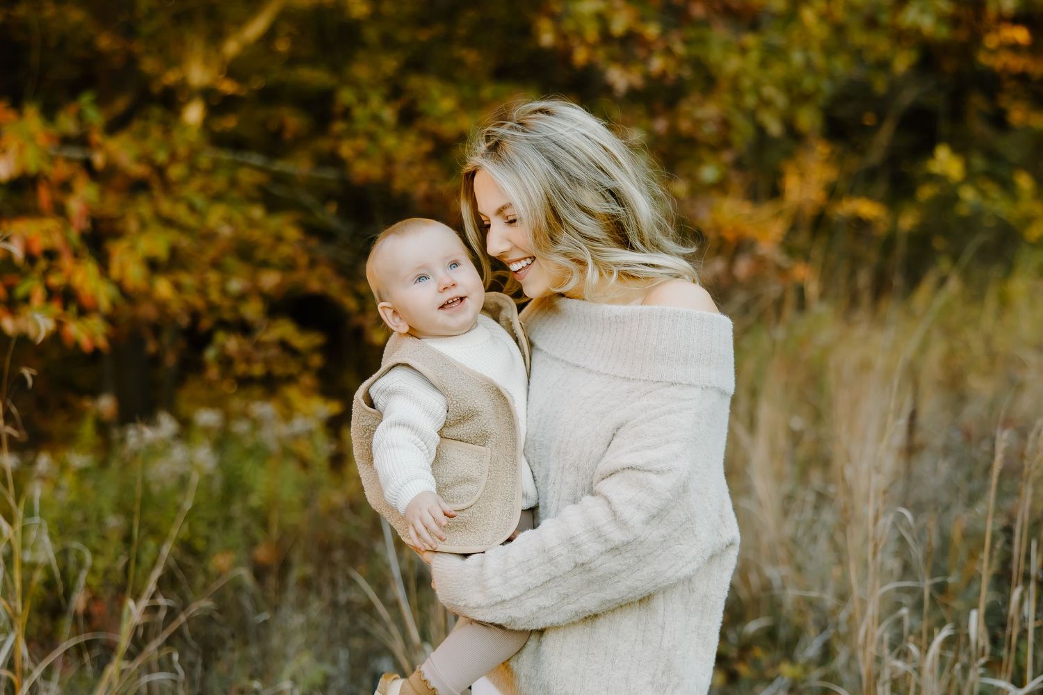 Mother and baby embracing in natural outdoor setting with fall colors.