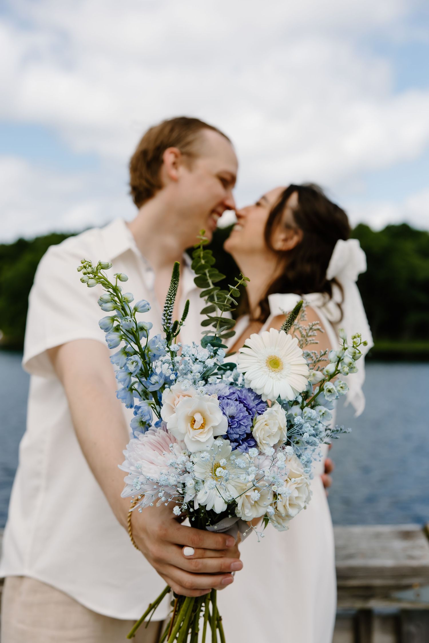 A tender moment shared between newlyweds with a stunning blue and white bouquet by the lake.