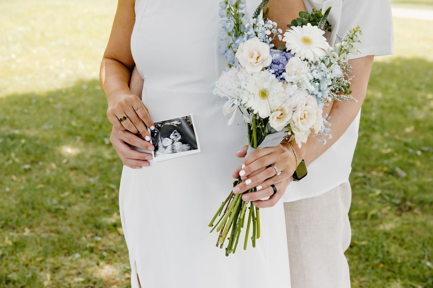 Romantic pregnancy announcement photos with white floral bouquet in an outdoor setting.