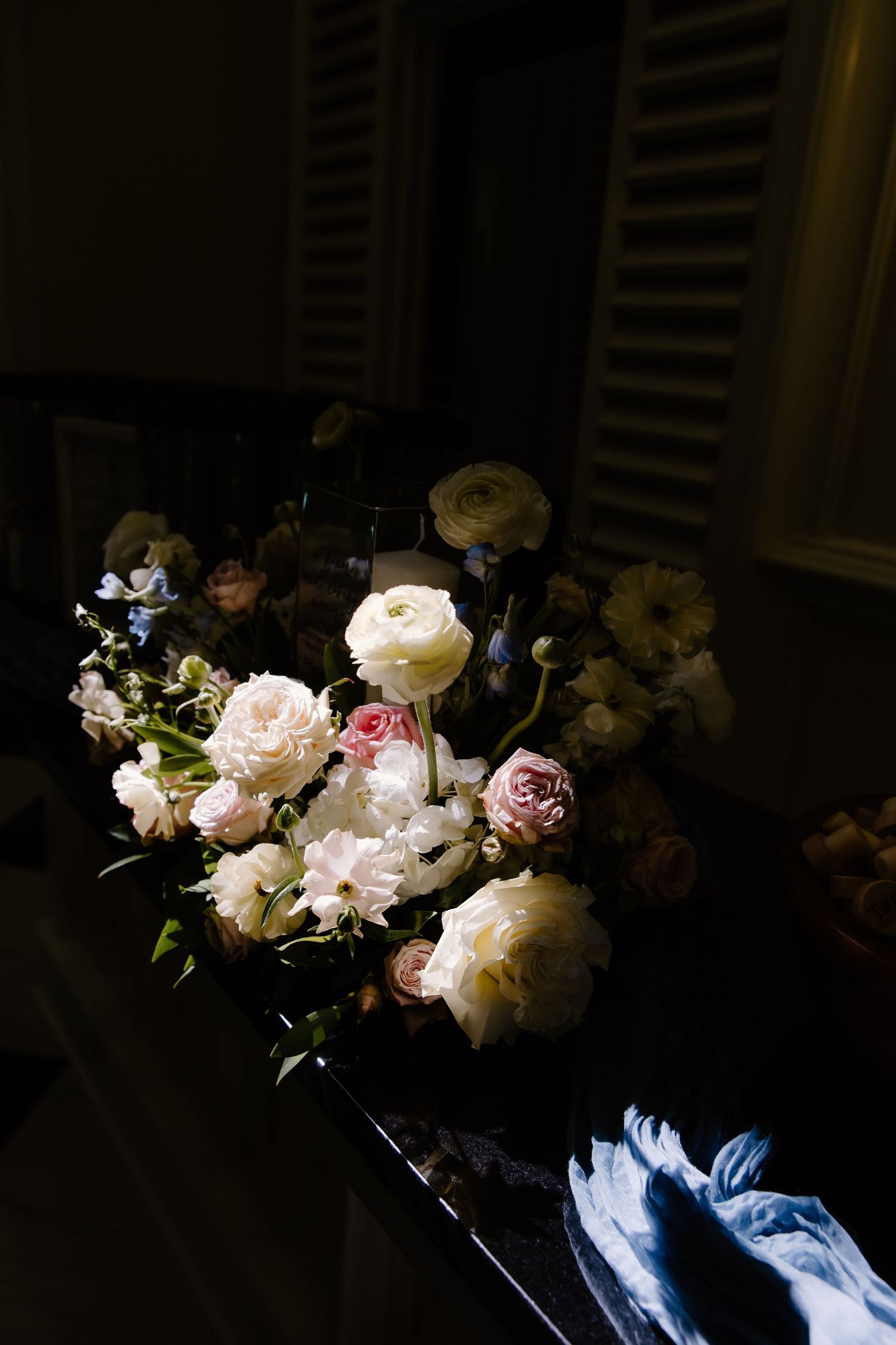 Dark moody still life photograph of pink and white peonies arranged with dramatic shadows and lighting.