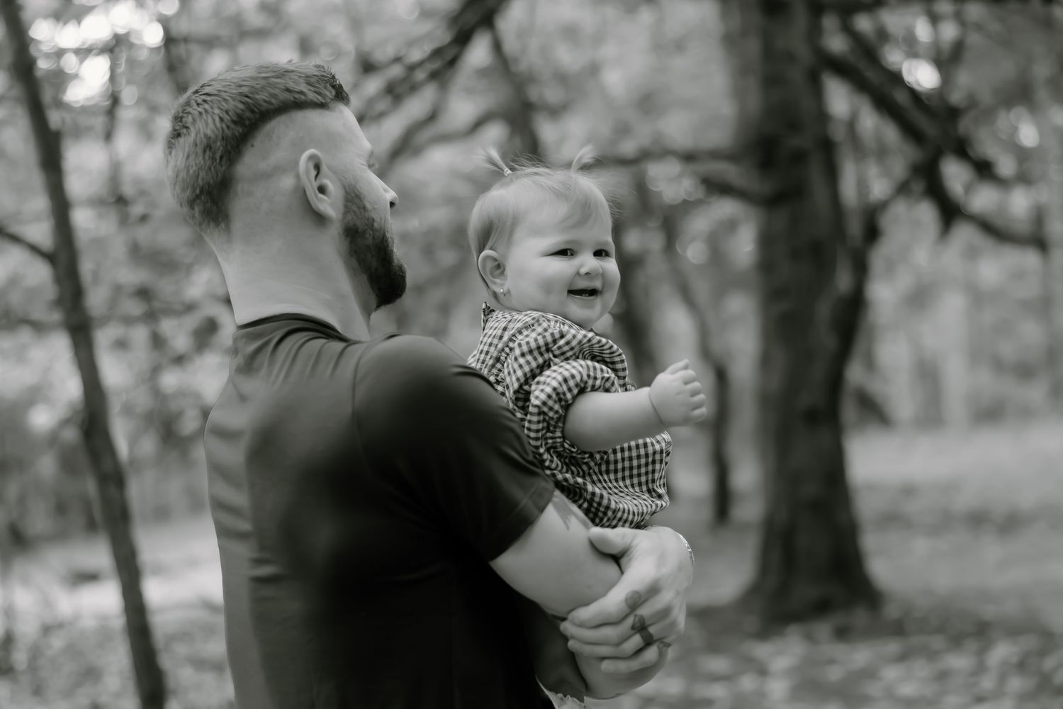Black and white portrait of parent and child sharing a tender moment in wooded setting.