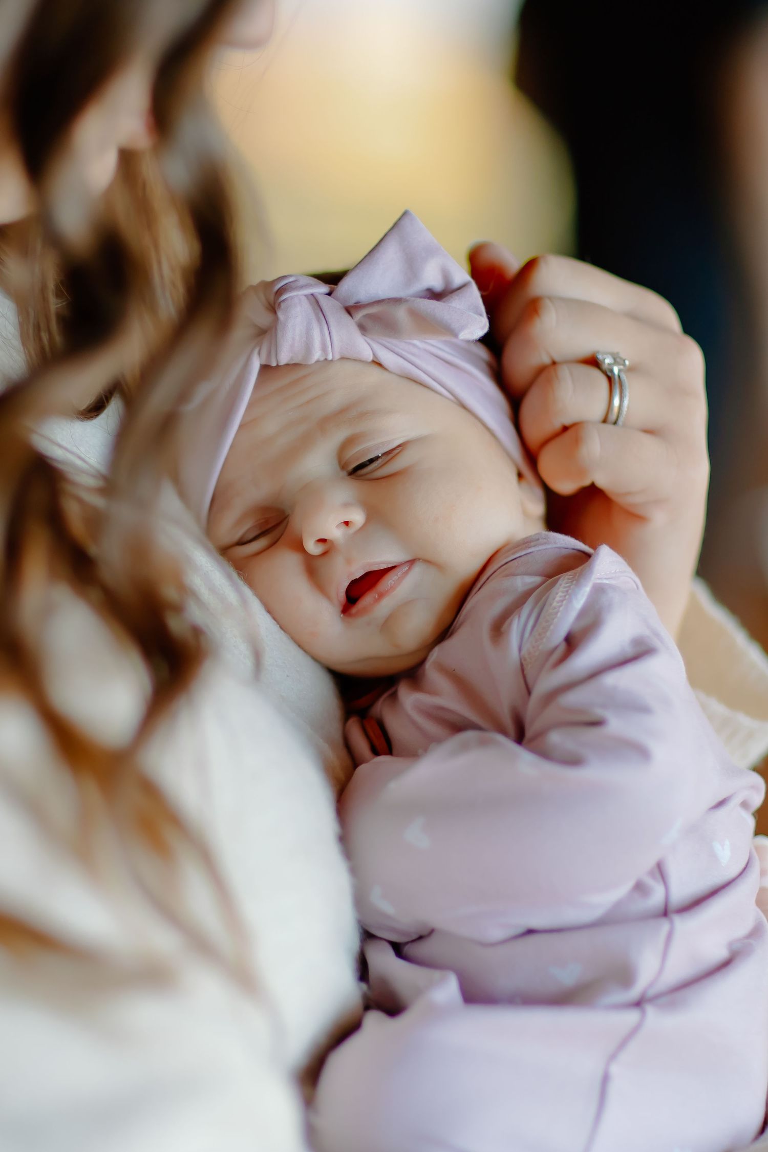 A sleeping baby in pink clothing and bow headband rests peacefully in loving arms.