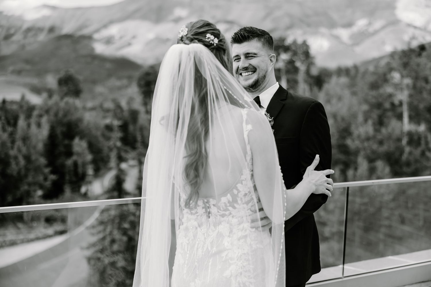 Black and white portrait of newlyweds sharing a joyful moment against mountain scenery.