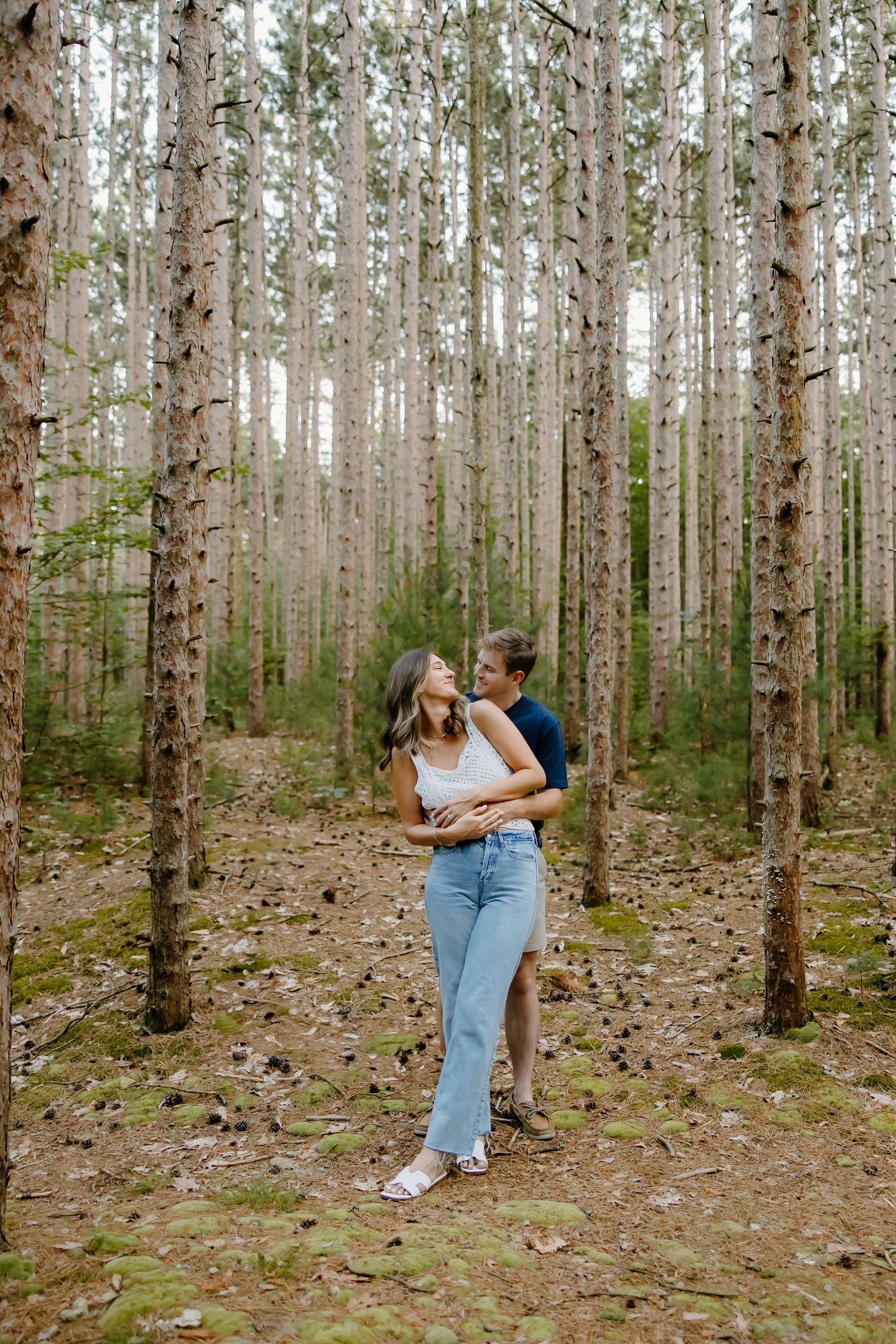 A couple poses among tall birch trees in a serene forest setting.