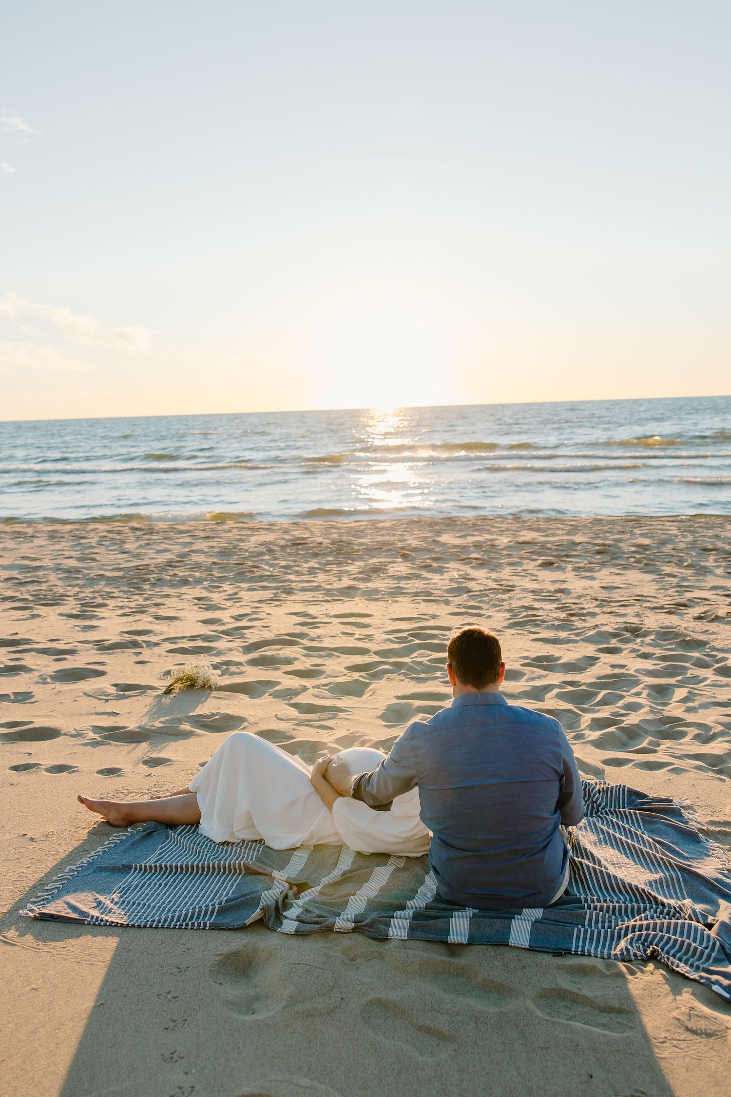 Two people relaxing on a striped blanket watching the sunset over the ocean.
