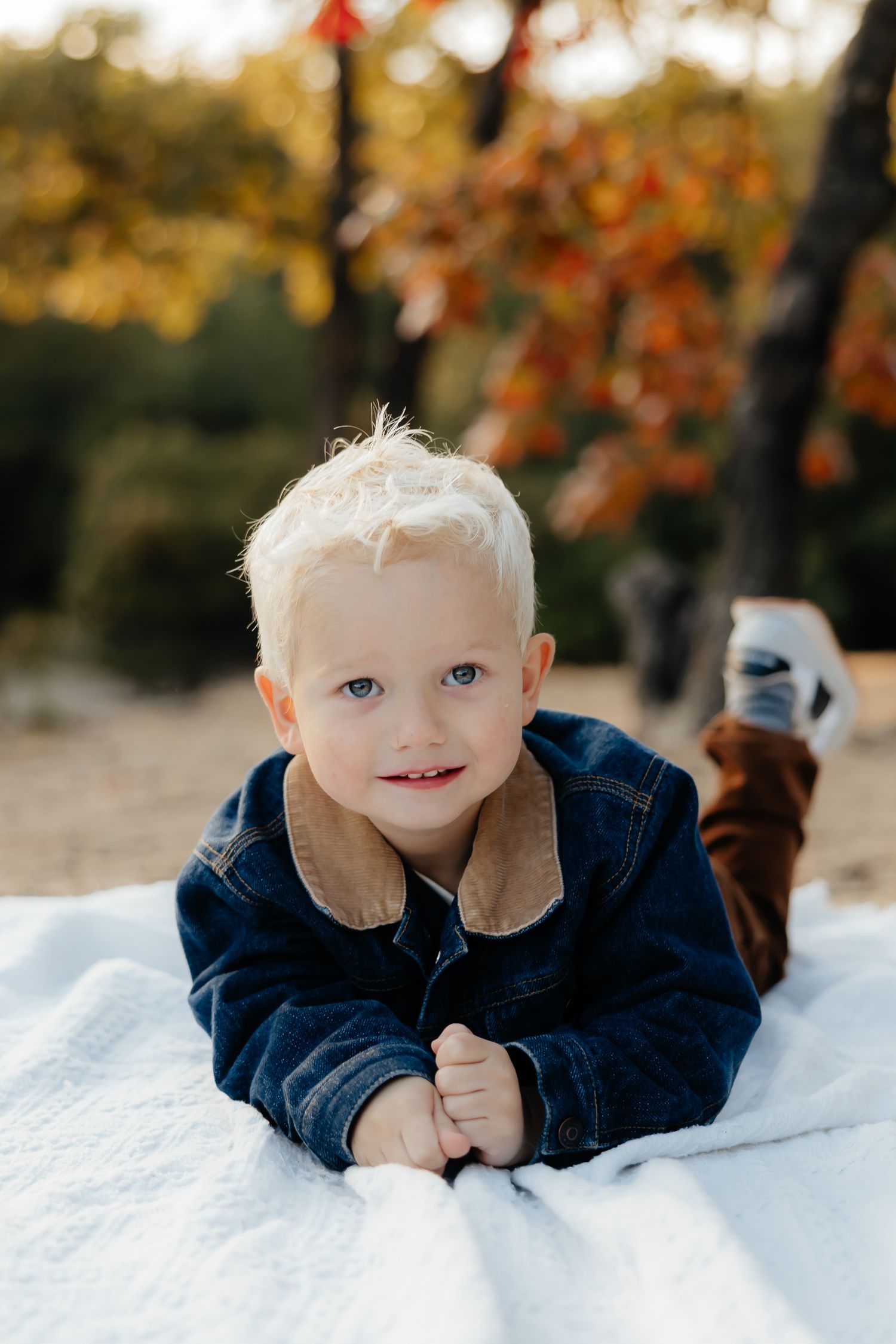 A young child in navy blue lies on a white blanket outdoors.