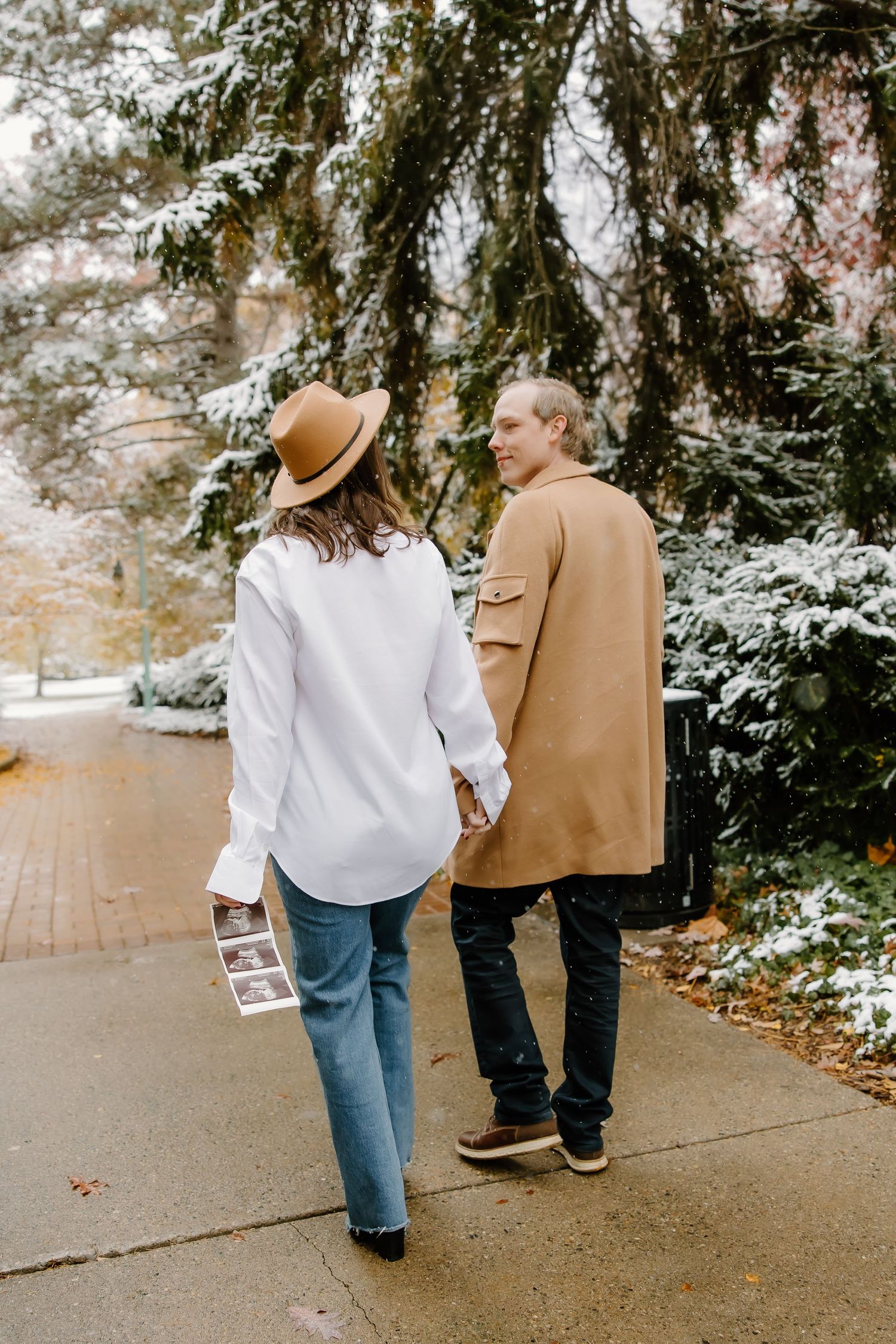Couple walking together in winter, wearing matching camel coats on snowy path.