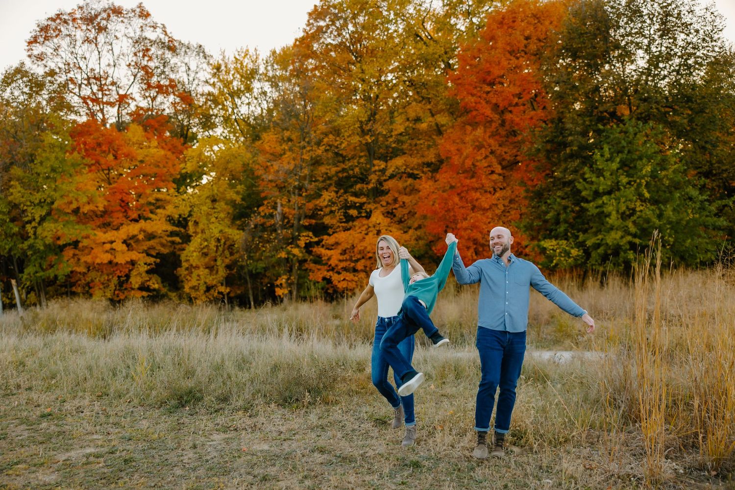 A group walks together through a scenic autumn meadow with vibrant orange and red fall foliage in the background.