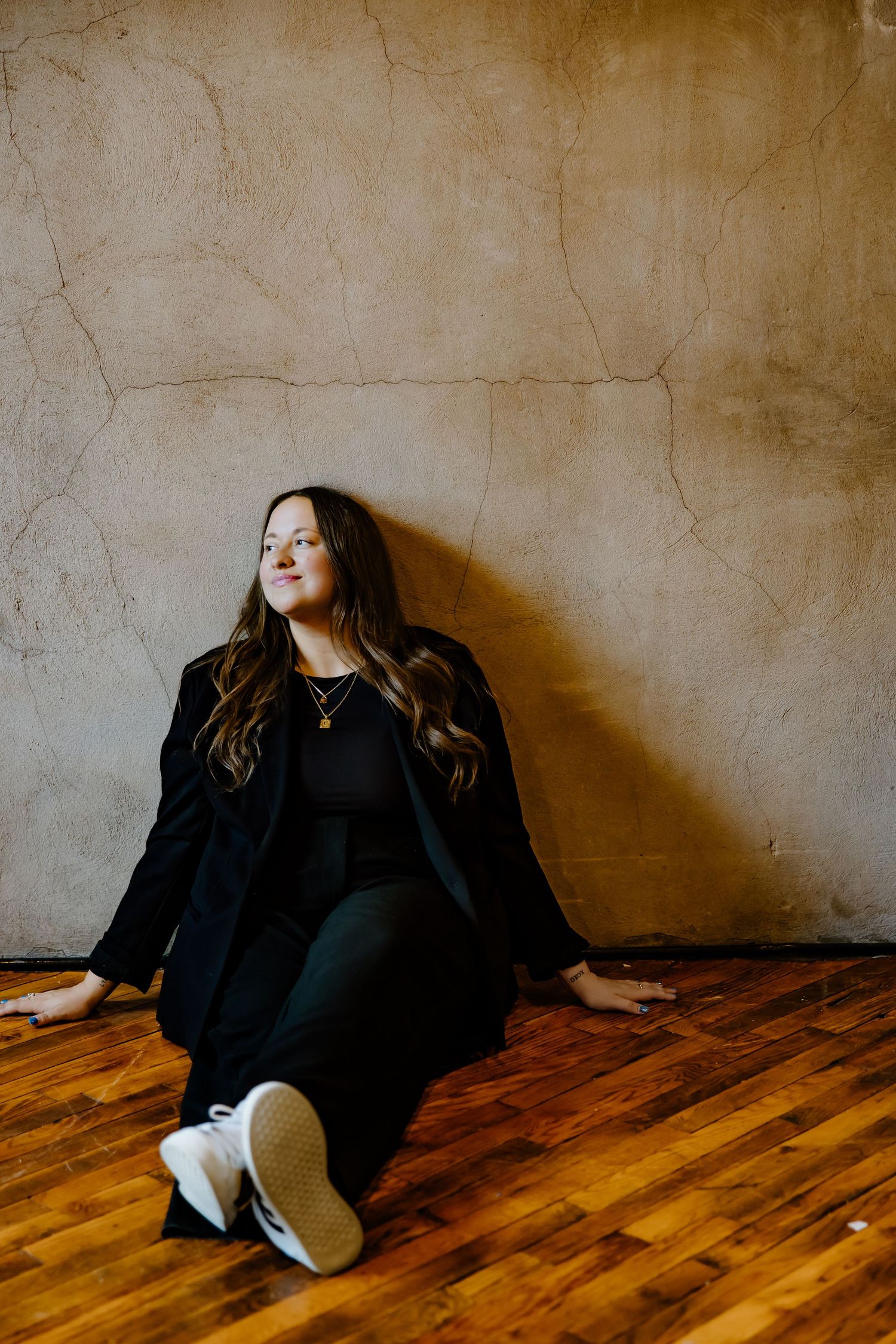 A figure in black clothing lies on a wooden floor against a textured beige wall in a progressive sequence of poses.