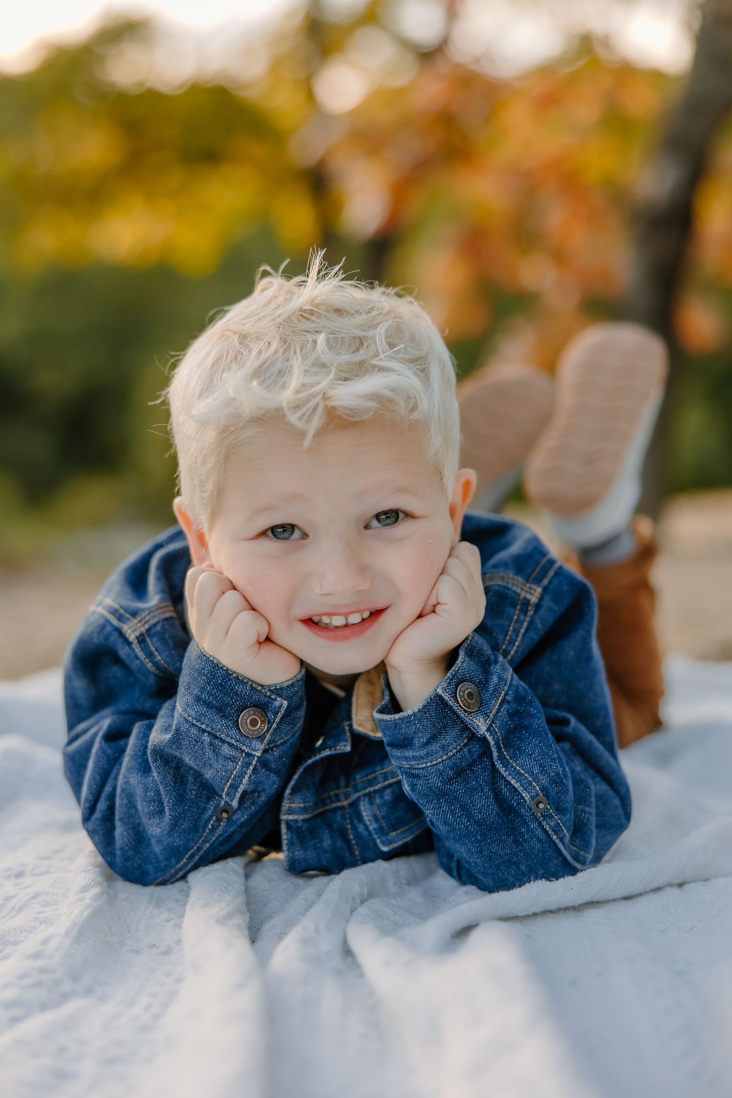 A small child in denim poses playfully on a white blanket outdoors.