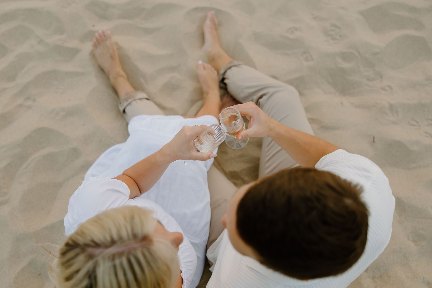 Overhead view of couple in white sitting on sandy beach.