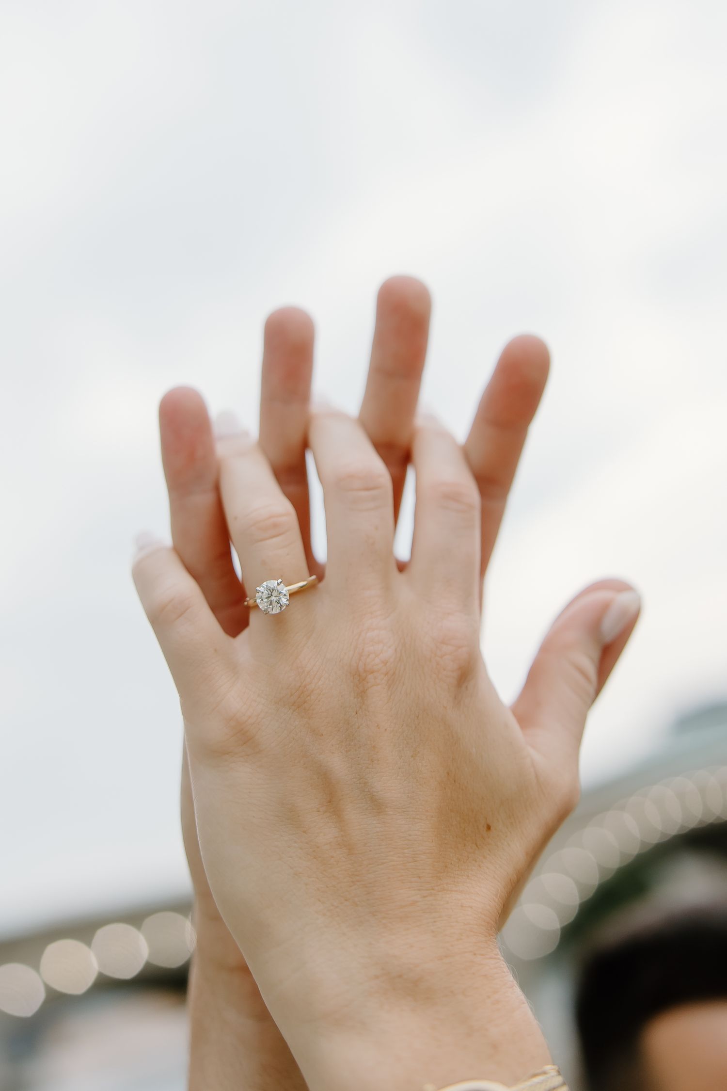 Close-up of engagement ring on hand against cloudy sky background.