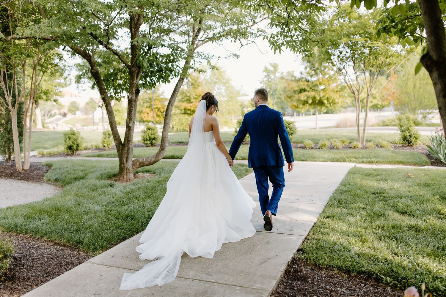 Newlyweds walk along a garden path with the bride's dress trailing behind them.