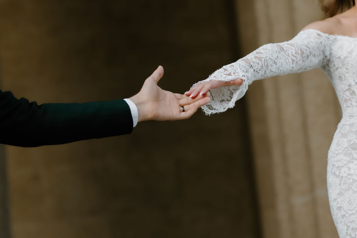 Bride and groom gently touching hands during wedding ceremony, bride wearing elegant lace long-sleeve gown.
