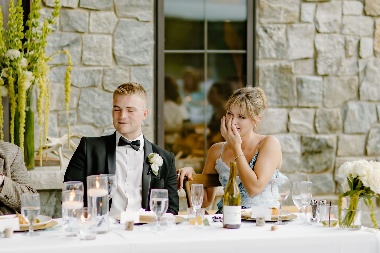 Wedding guests enjoy an elegant outdoor reception dinner at stone venue with white table settings.