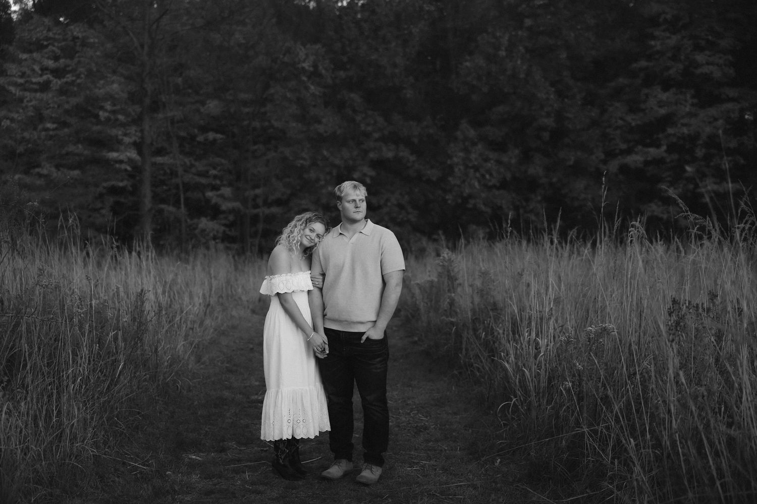 Black and white photo of a couple walking through a field with dramatic lighting and tall grass.
