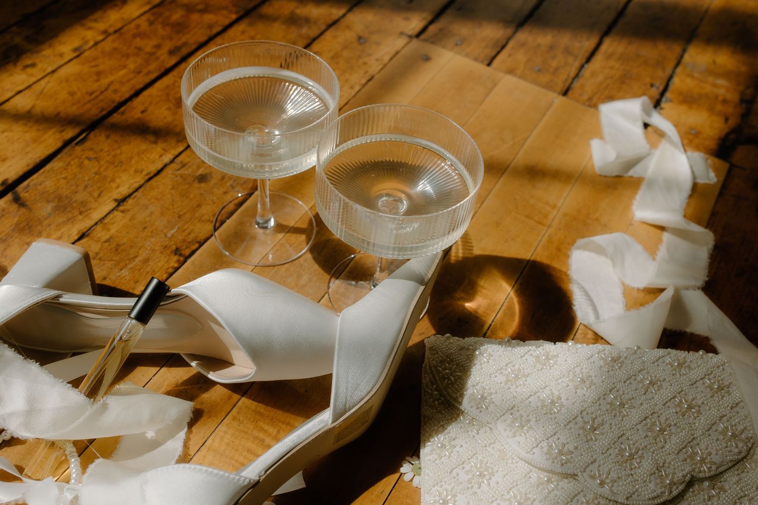 Champagne glasses and wedding details arranged on a rustic wooden table in warm lighting.