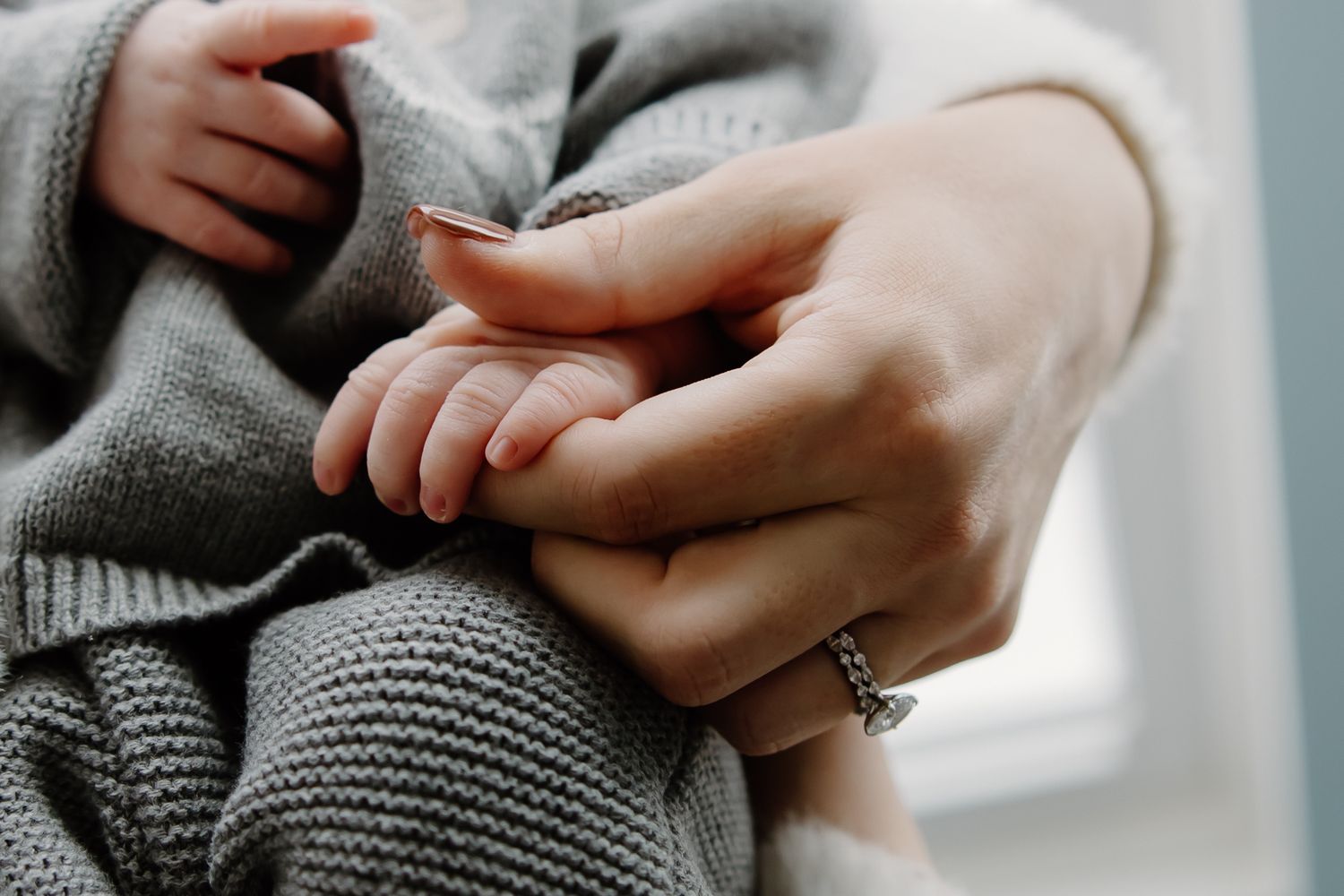 Detail shot of hands holding a tiny newborn wrapped in soft gray knitwear.