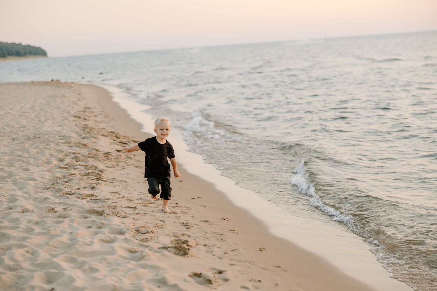 Family playing and splashing in the ocean waves at sunset along a peaceful beach.