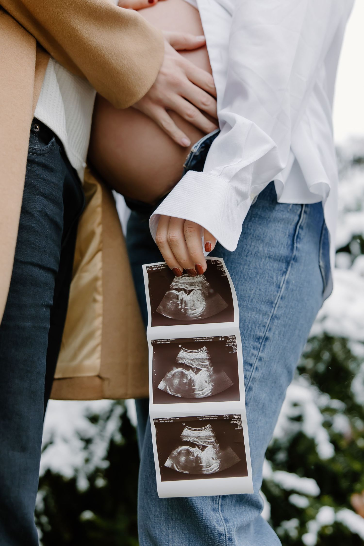 Hands holding ultrasound photos against a blurred background showing a pregnancy announcement moment.