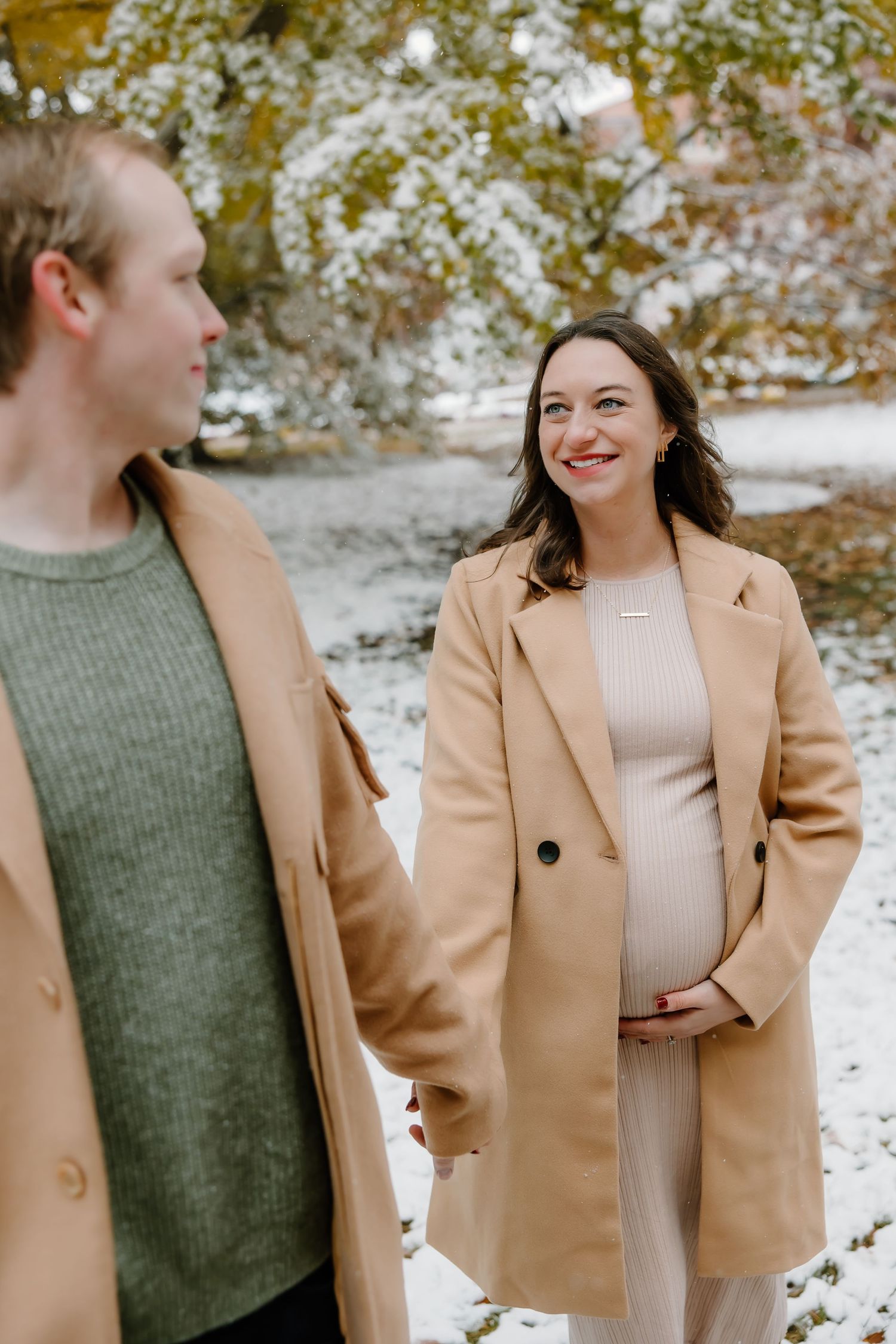 Winter maternity session featuring couple in coordinated casual wear against snowy backdrop.