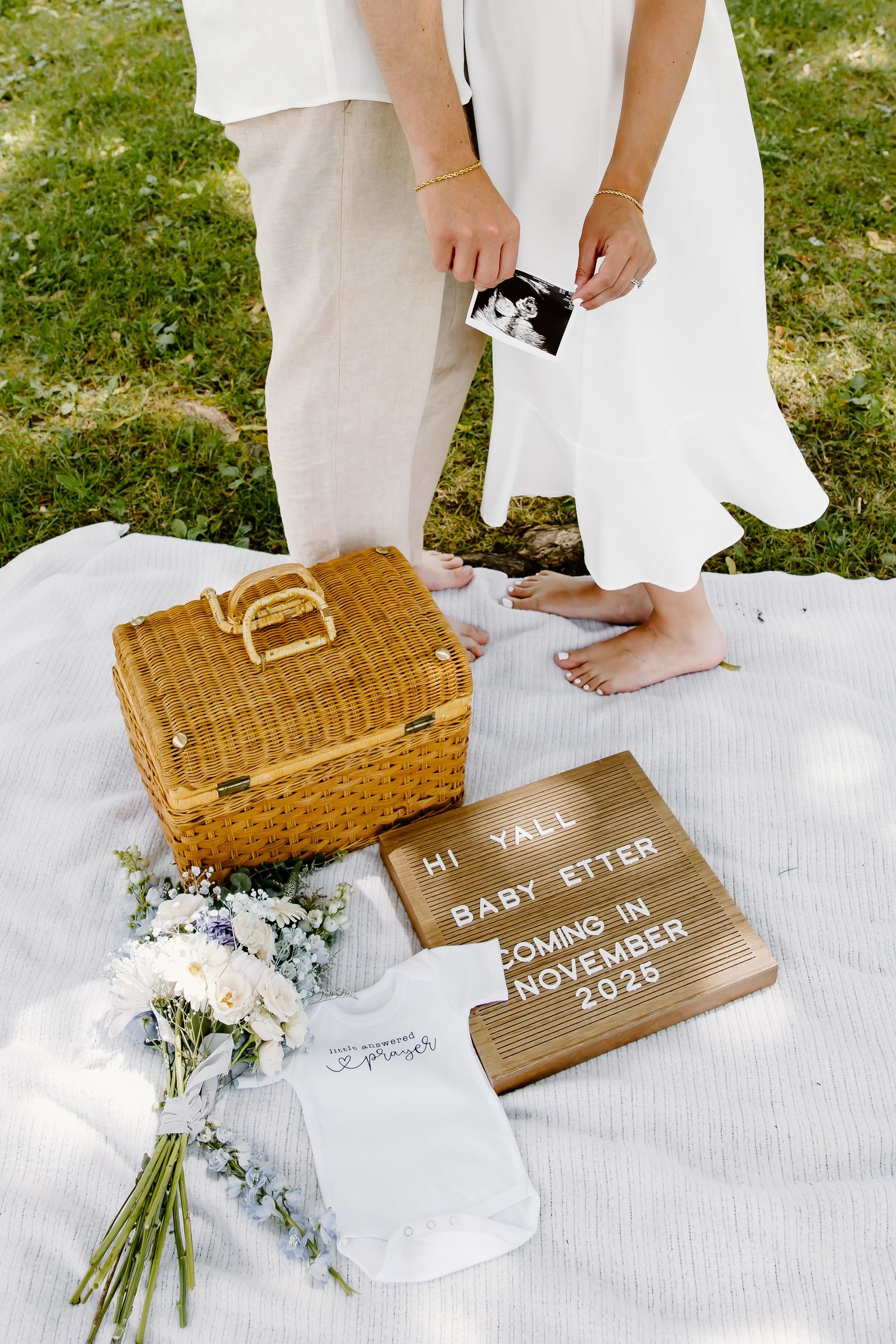 Wooden signs and wicker basket arranged with flowers for baby announcement photo shoot.