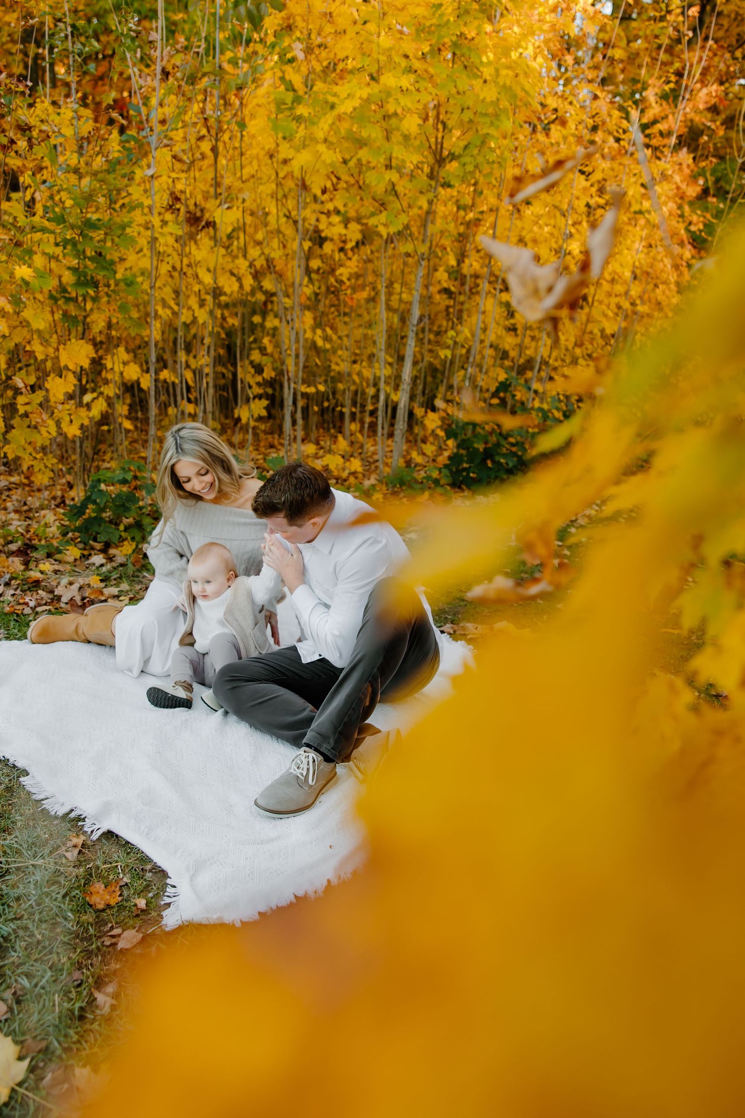 Family resting on white blanket surrounded by golden autumn foliage.