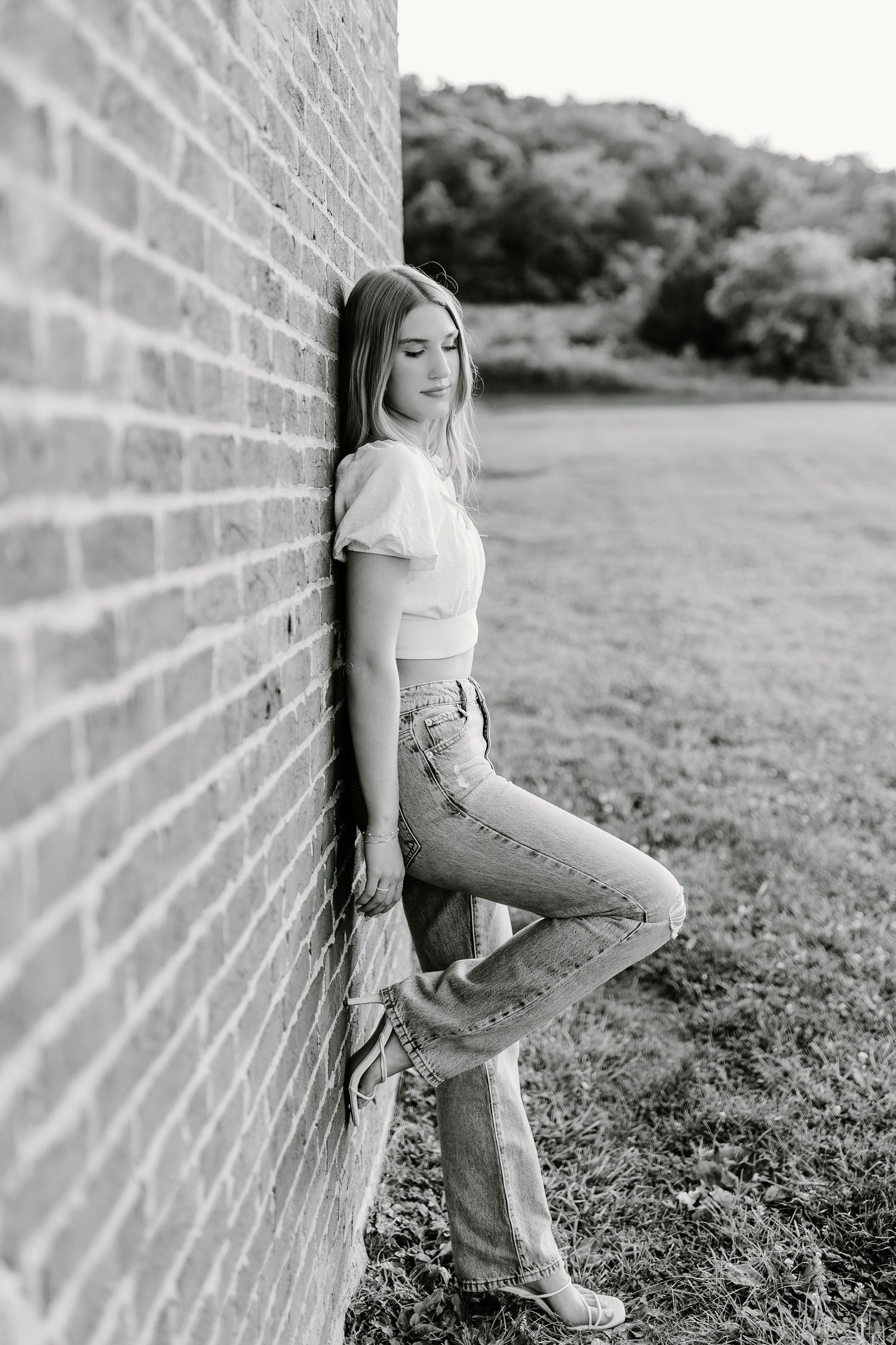 Artistic black and white portrait against a rustic brick wall in a rural setting.