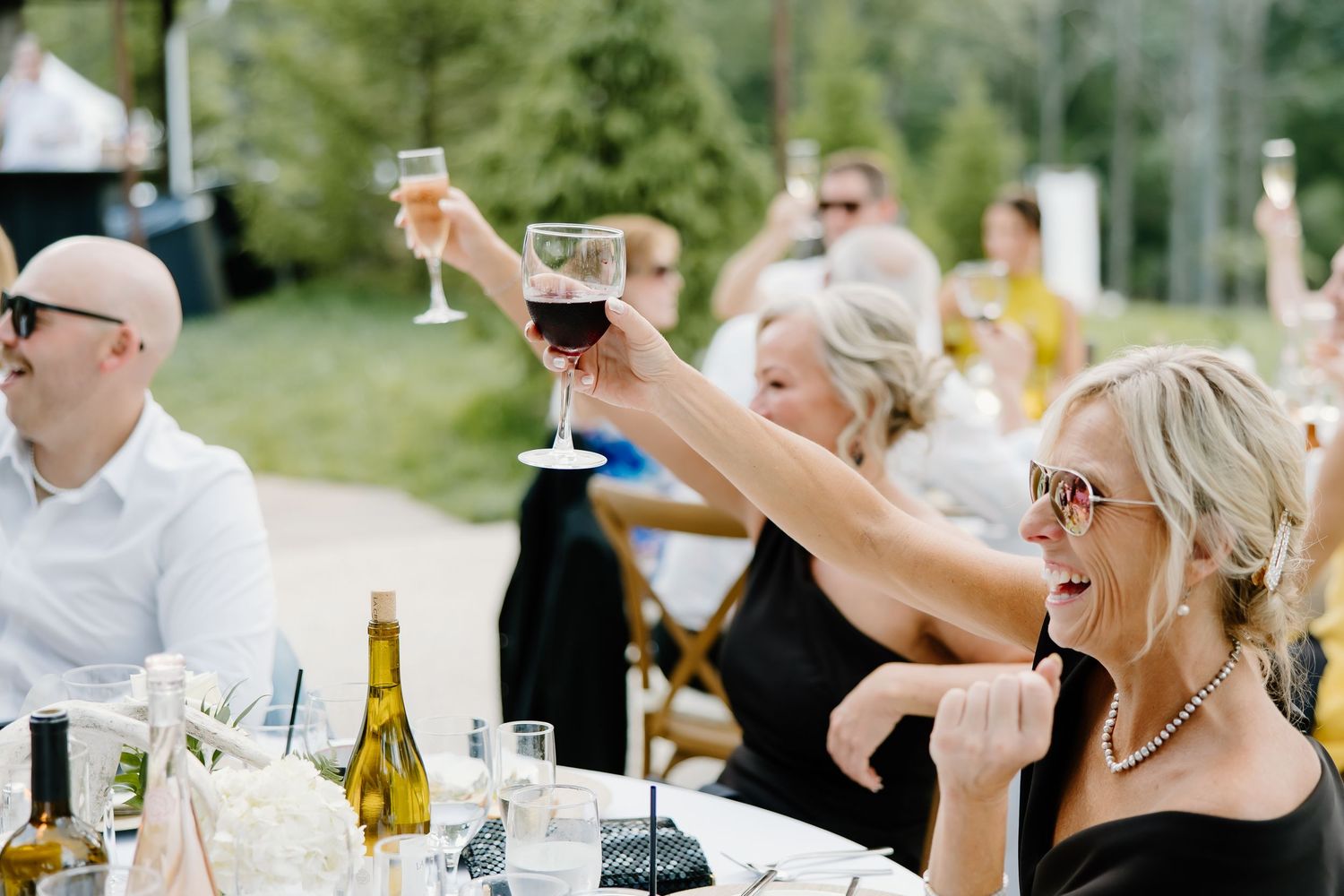 Wedding guests raise champagne glasses in celebration at an outdoor summer reception.