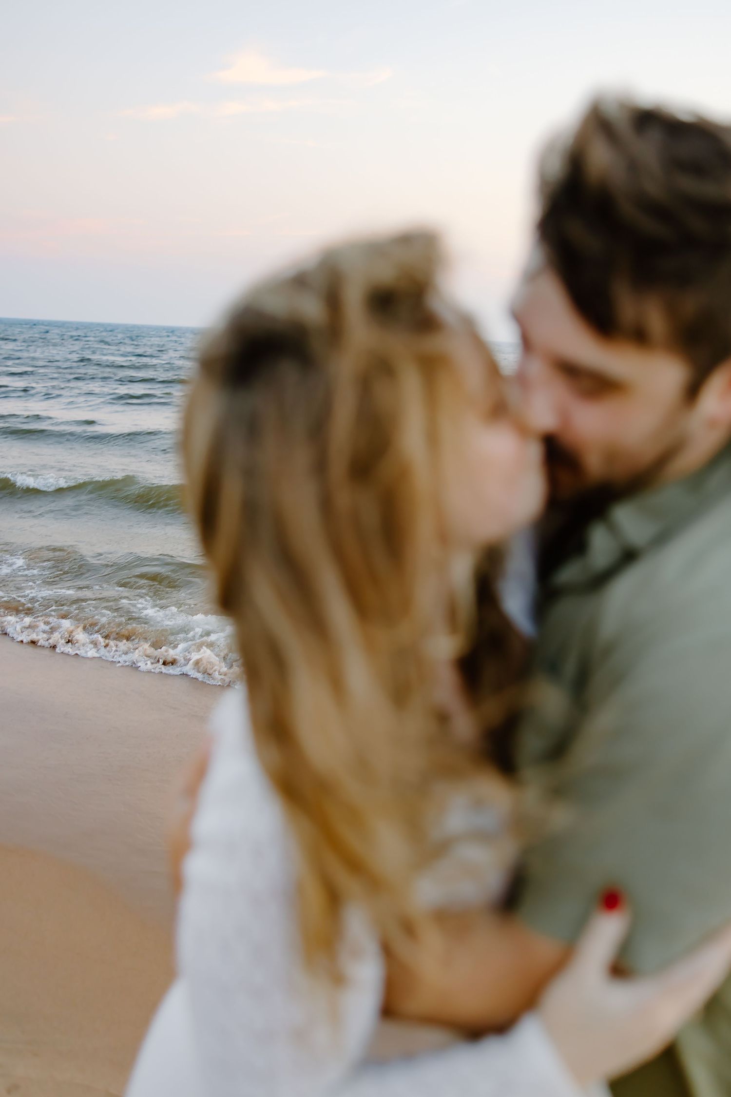 Intimate beach moment captured with ocean waves and sunset in background.
