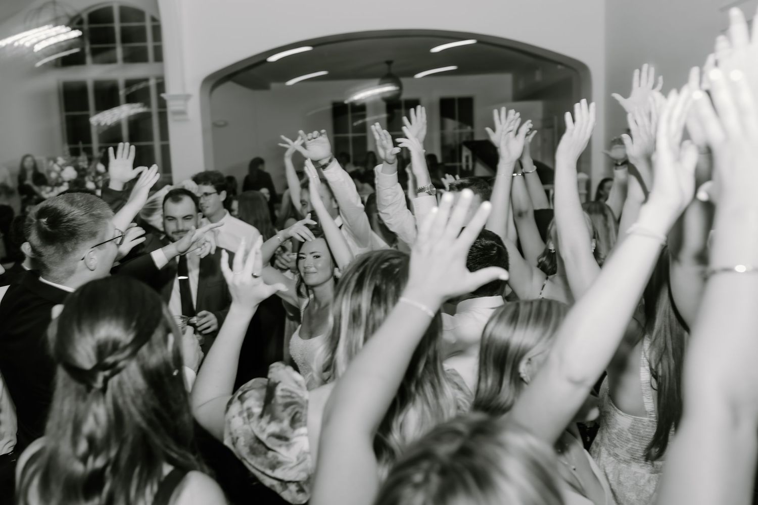 Black and white photo of wedding reception crowd with hands raised in celebration.