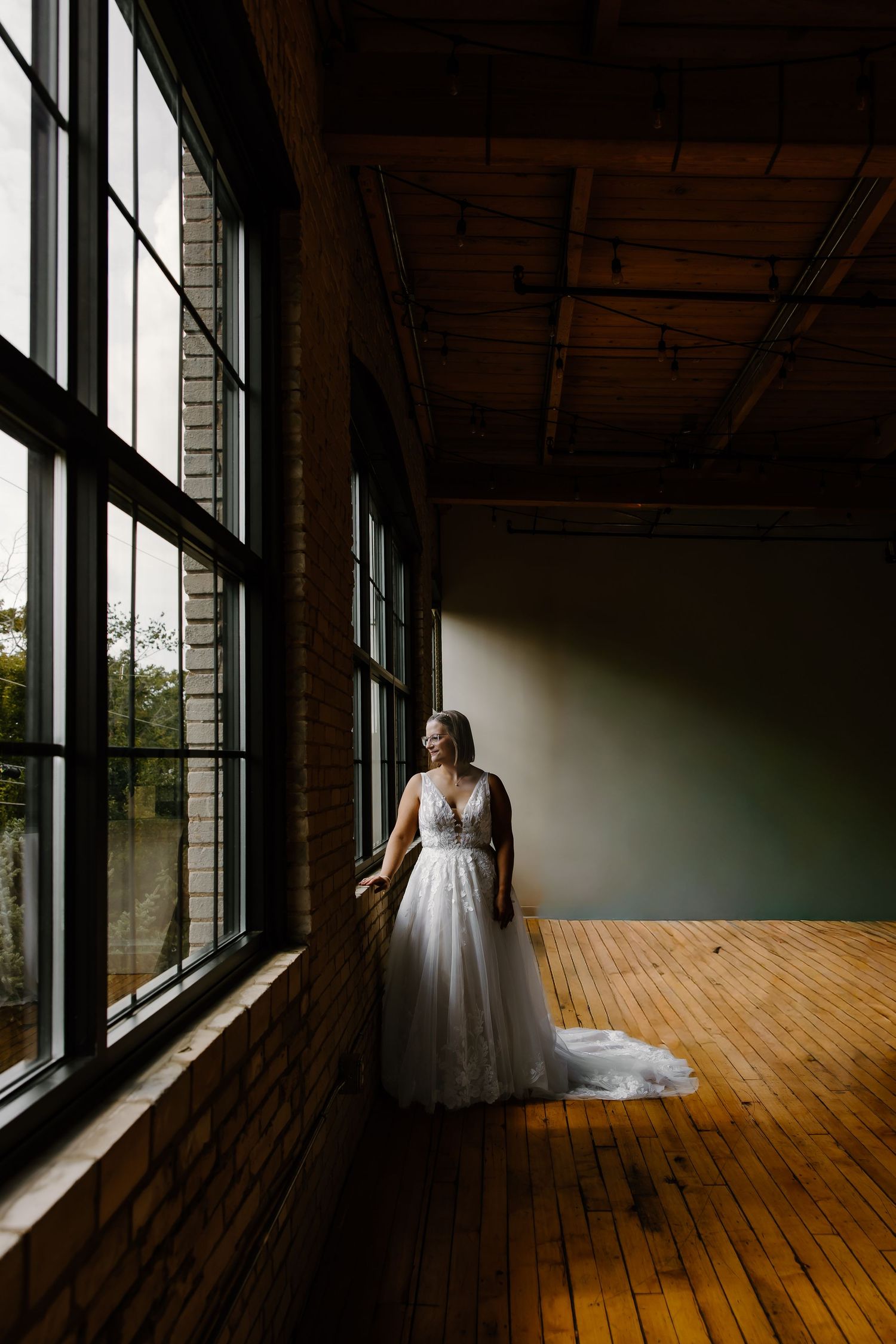 Sunlight streams through large windows onto a hardwood floor where a white wedding dress creates dramatic shadows.