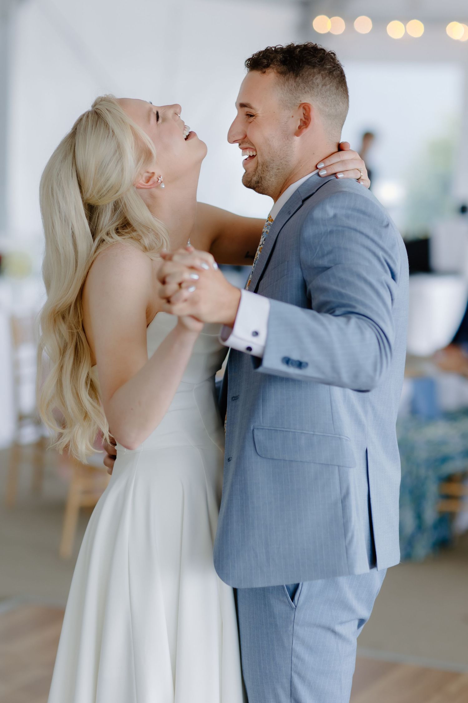 Bride and groom share a joyful first dance, laughing together at their elegant wedding reception.