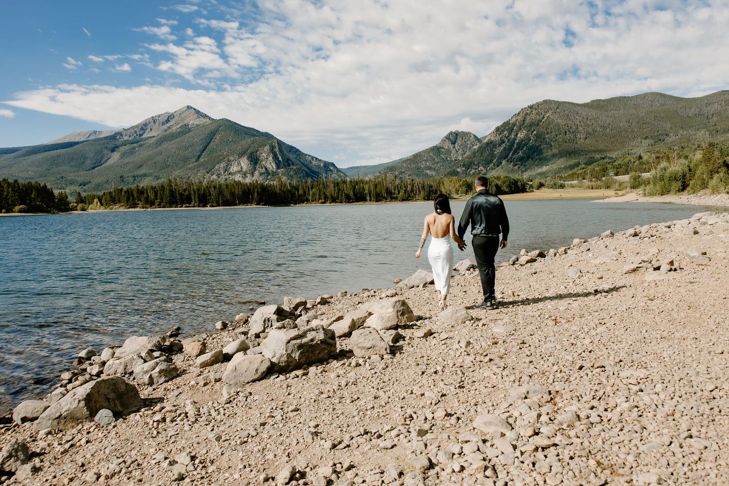 Mountain lake panorama with rocky shoreline and distant peaks under cloudy skies.