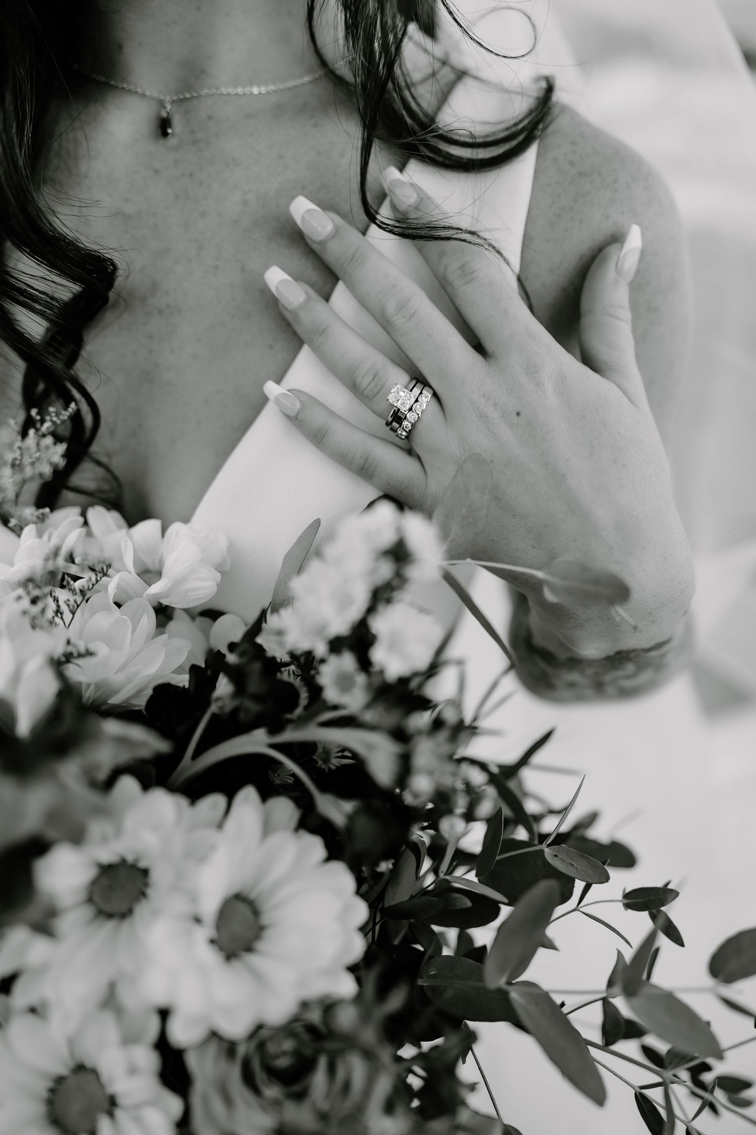 Close-up of bride's hands with wedding ring and floral bouquet in black and white.