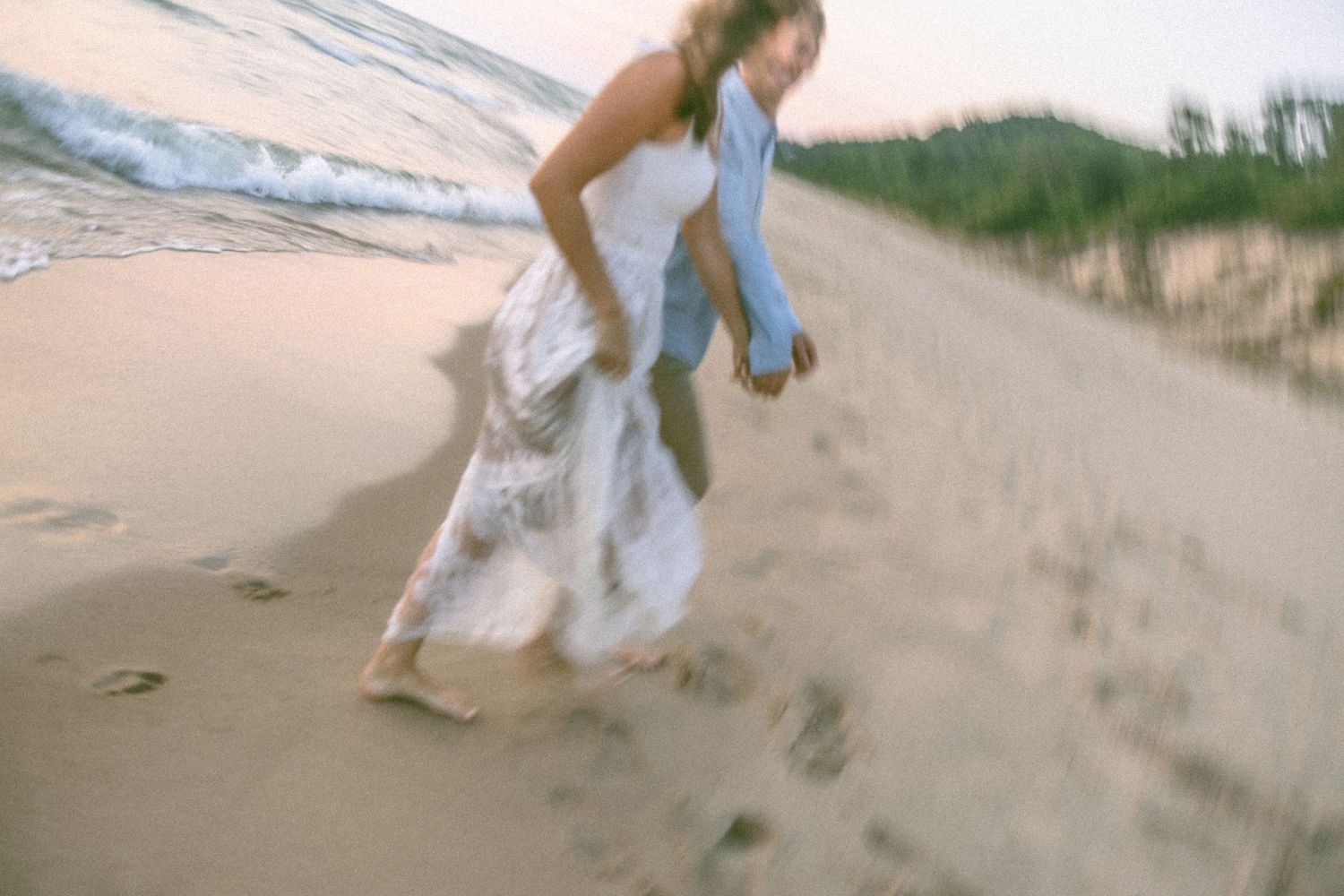 Motion-blurred figure in white dress running along beach at sunset.