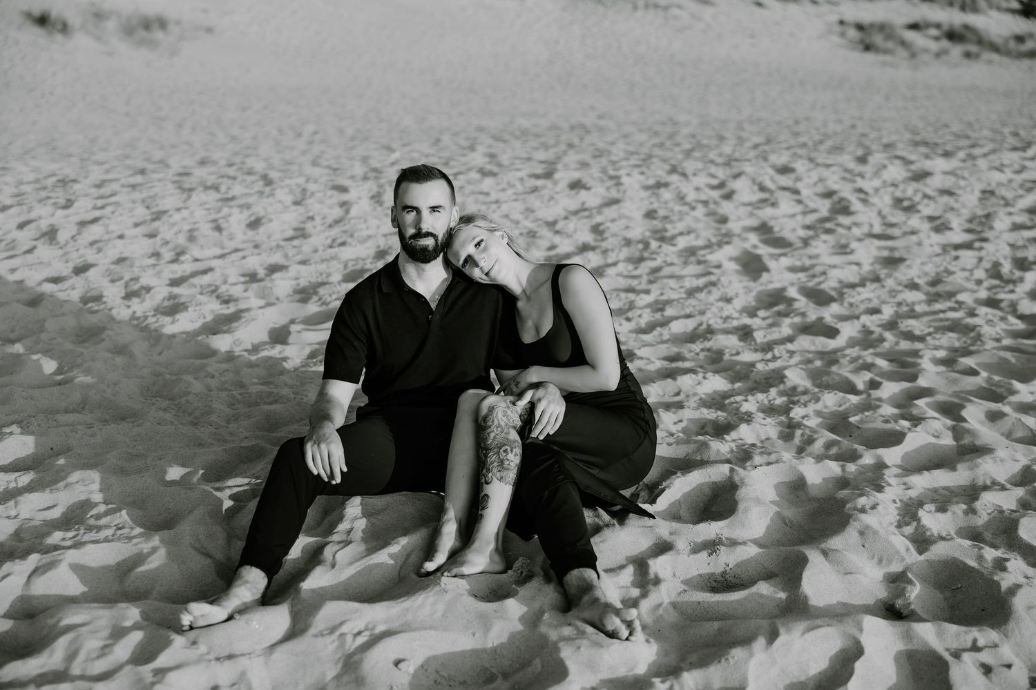 Black and white photo of couple relaxing together on sandy beach.