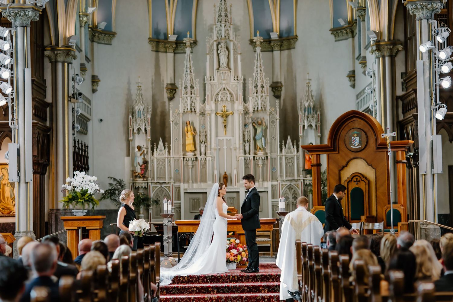 Gothic cathedral interior with dramatic lighting and red carpeted altar steps during a wedding ceremony.