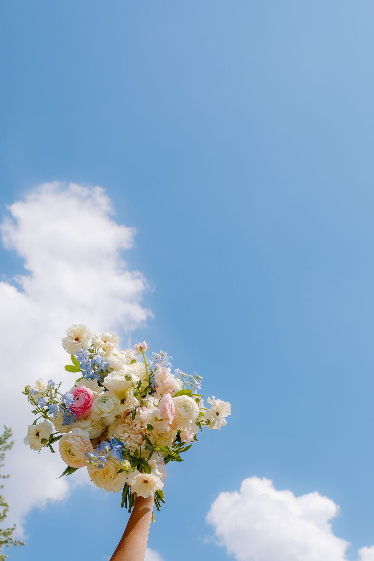 White floral bouquet held up against a bright blue sky with fluffy clouds.