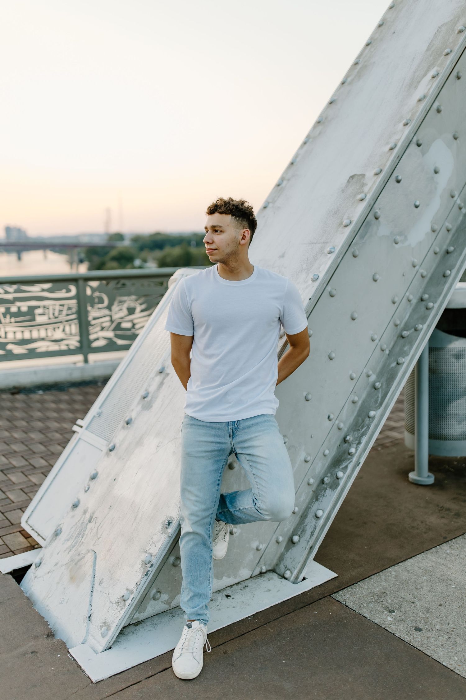 Side profile portrait against industrial architecture wearing light casual clothing.
