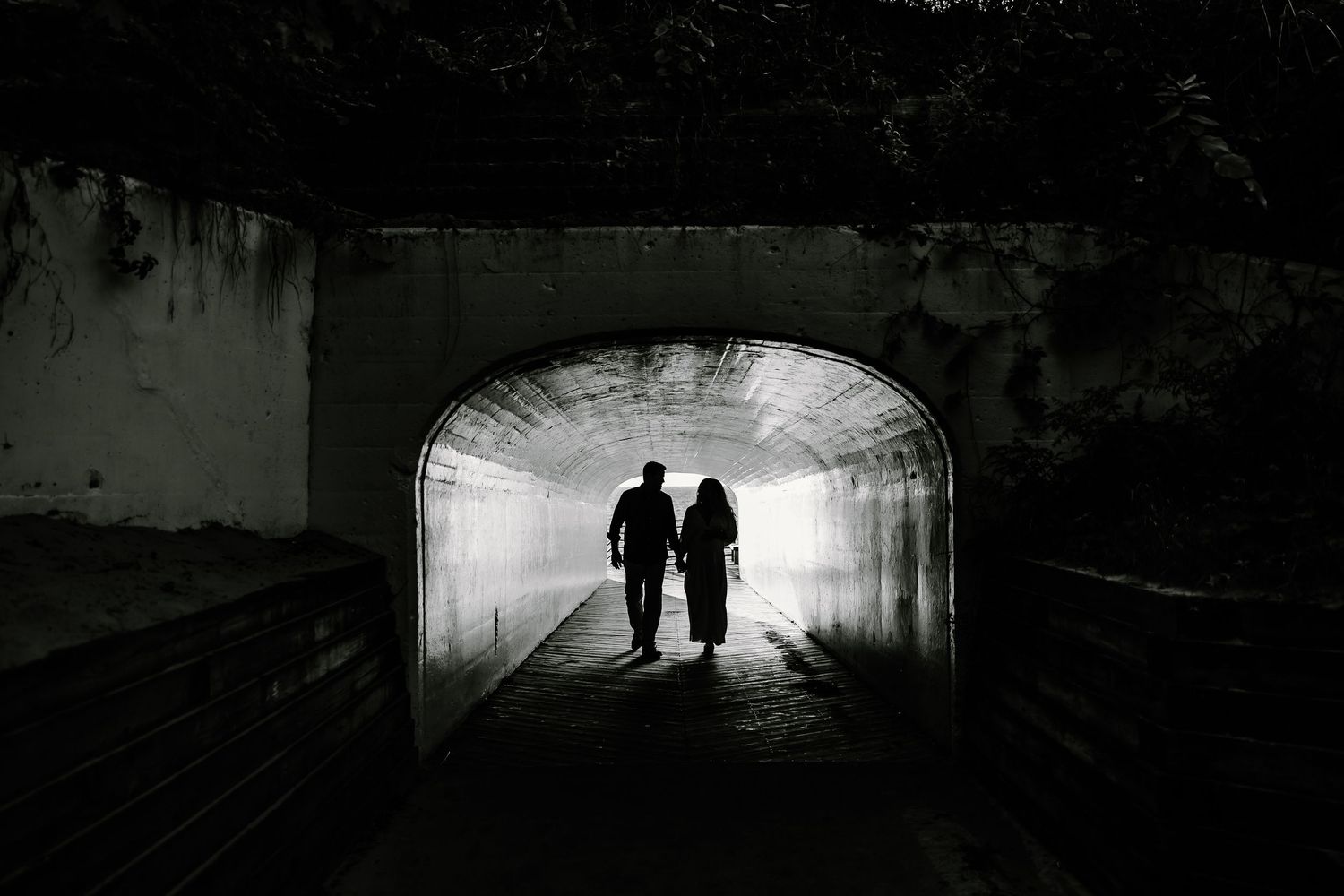 Two figures in silhouette walking through illuminated tunnel passage.