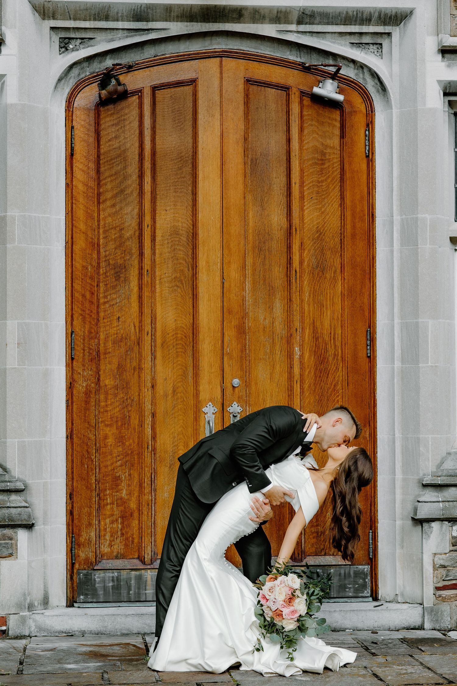 Romantic wedding portrait in front of ornate wooden church doors.