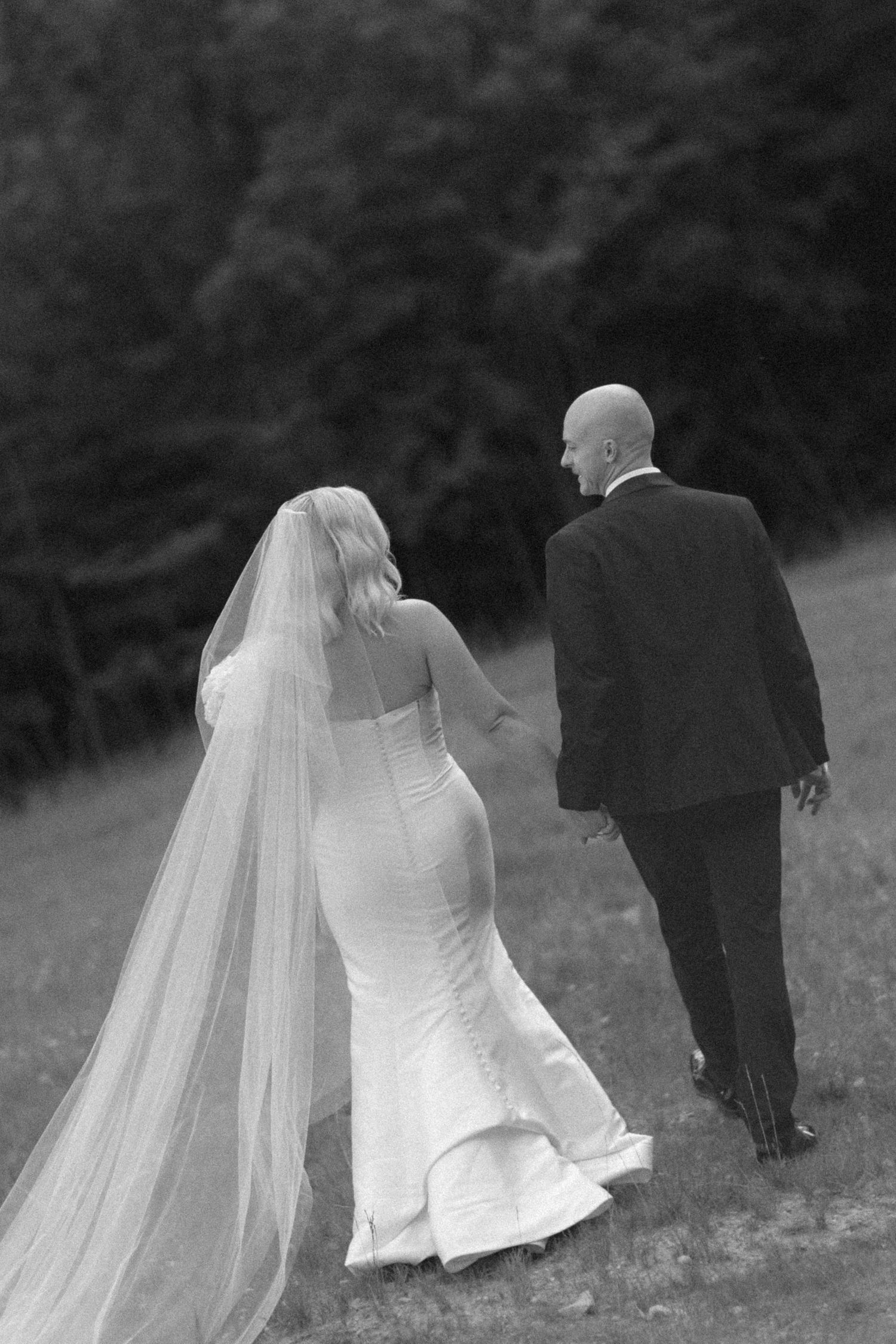 Black and white photo of newlyweds walking together through a garden setting.