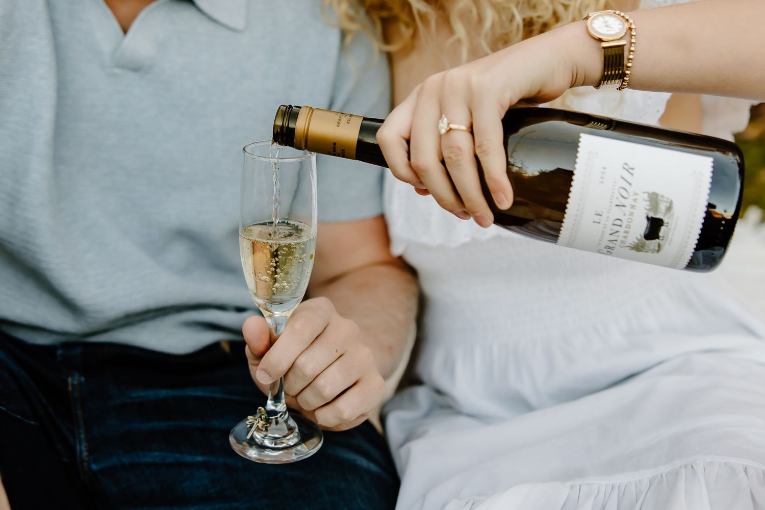 Hands pouring and holding champagne glasses during outdoor celebration.