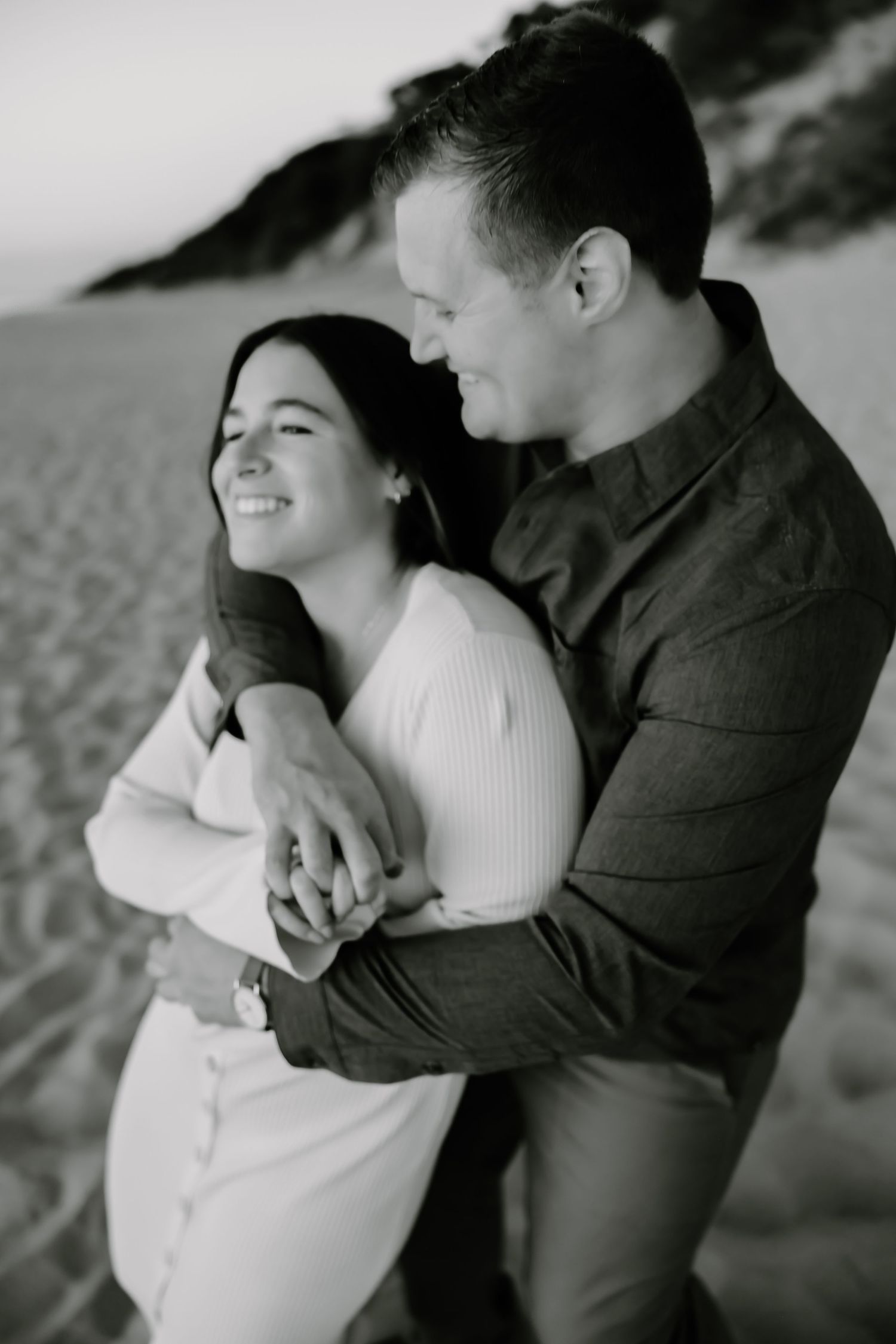 Black and white photo of couple embracing on beach during engagement session.