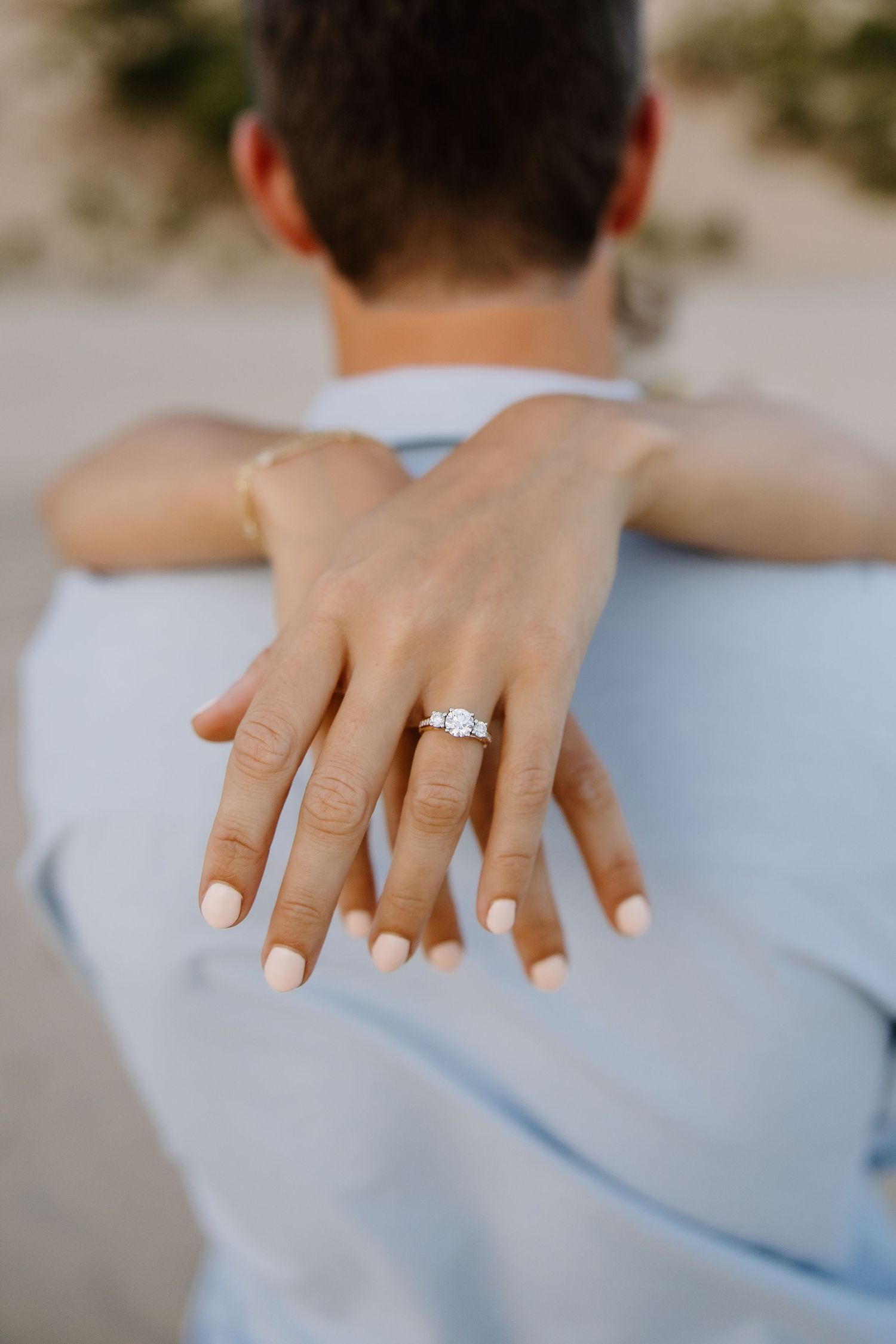 Close-up of hand with engagement ring resting on shoulder in soft lighting.