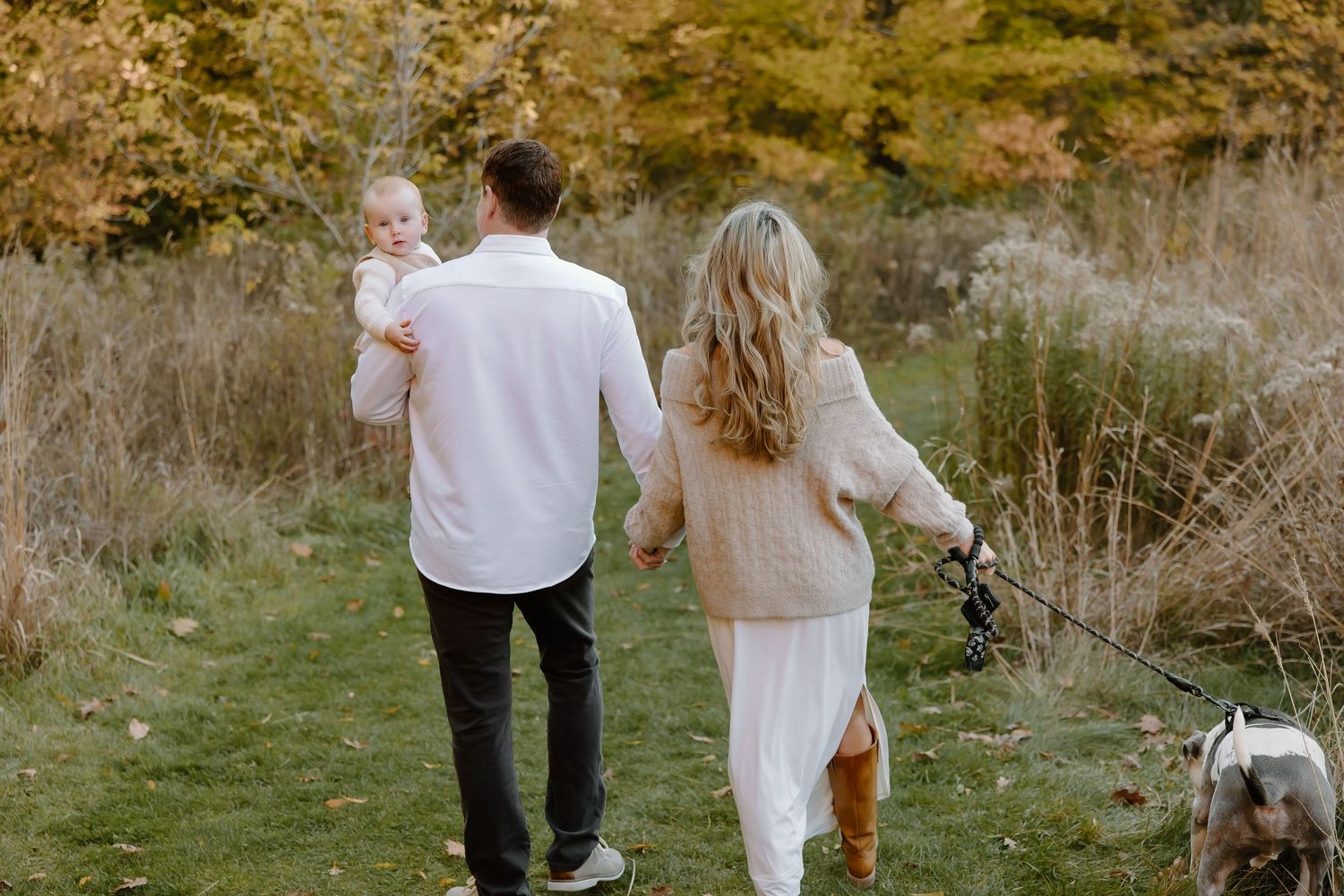 Family walking together through a field with golden autumn trees in the background.