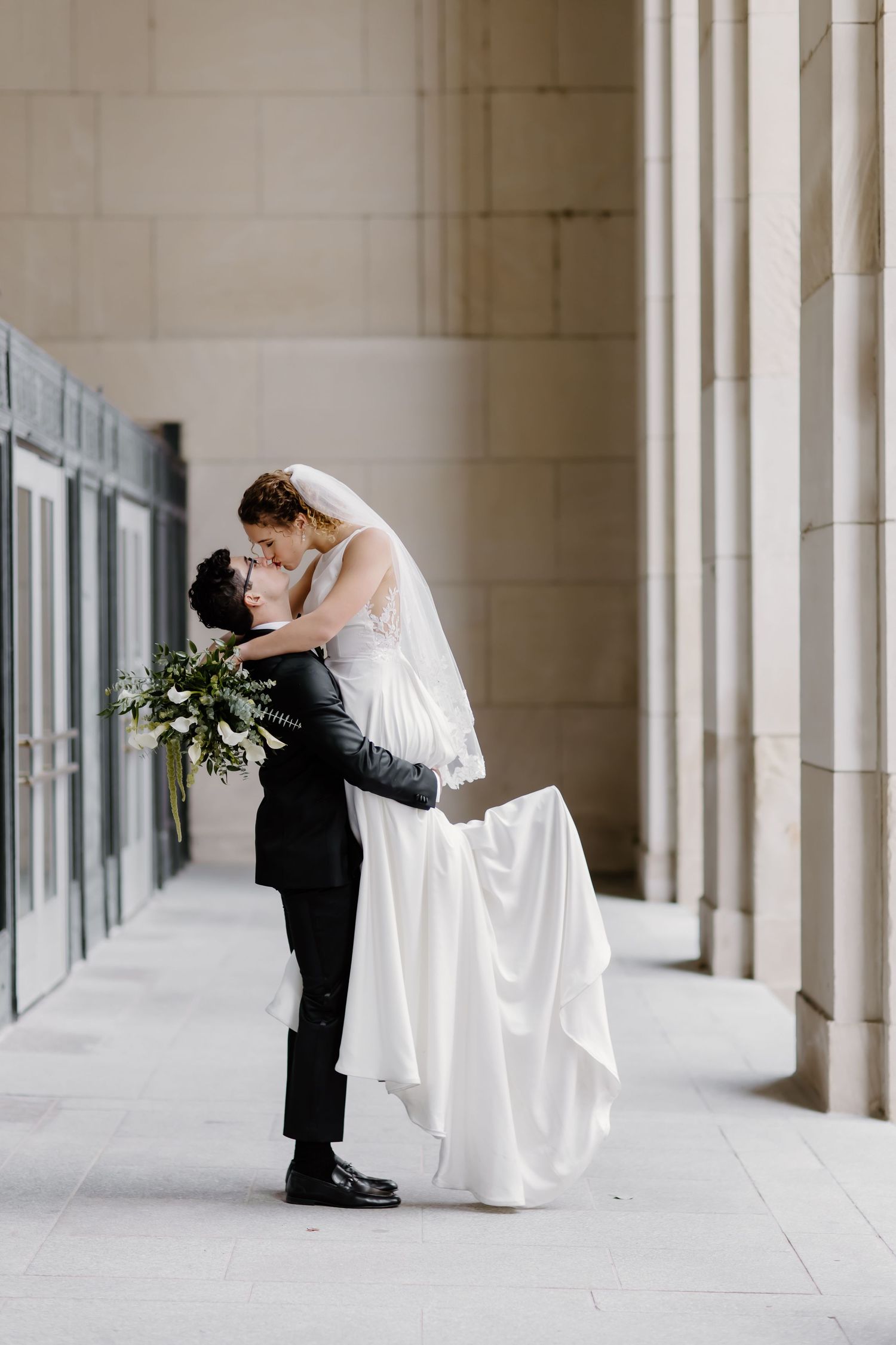 Elegant wedding couple embracing in a white columned hallway.