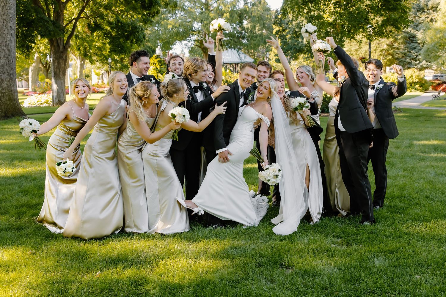 Wedding party relaxes together on grass in formal attire during golden hour.